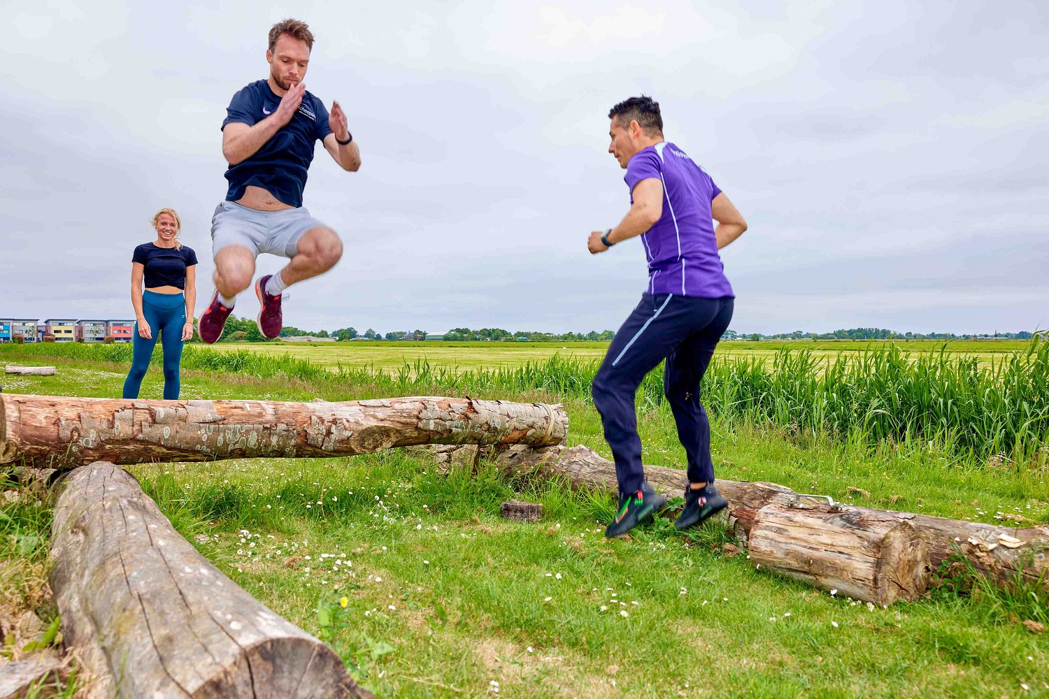 Bootcamp bij OHC Soest. Man springt over boomstam en wordt aangemoedigd door instructeur.