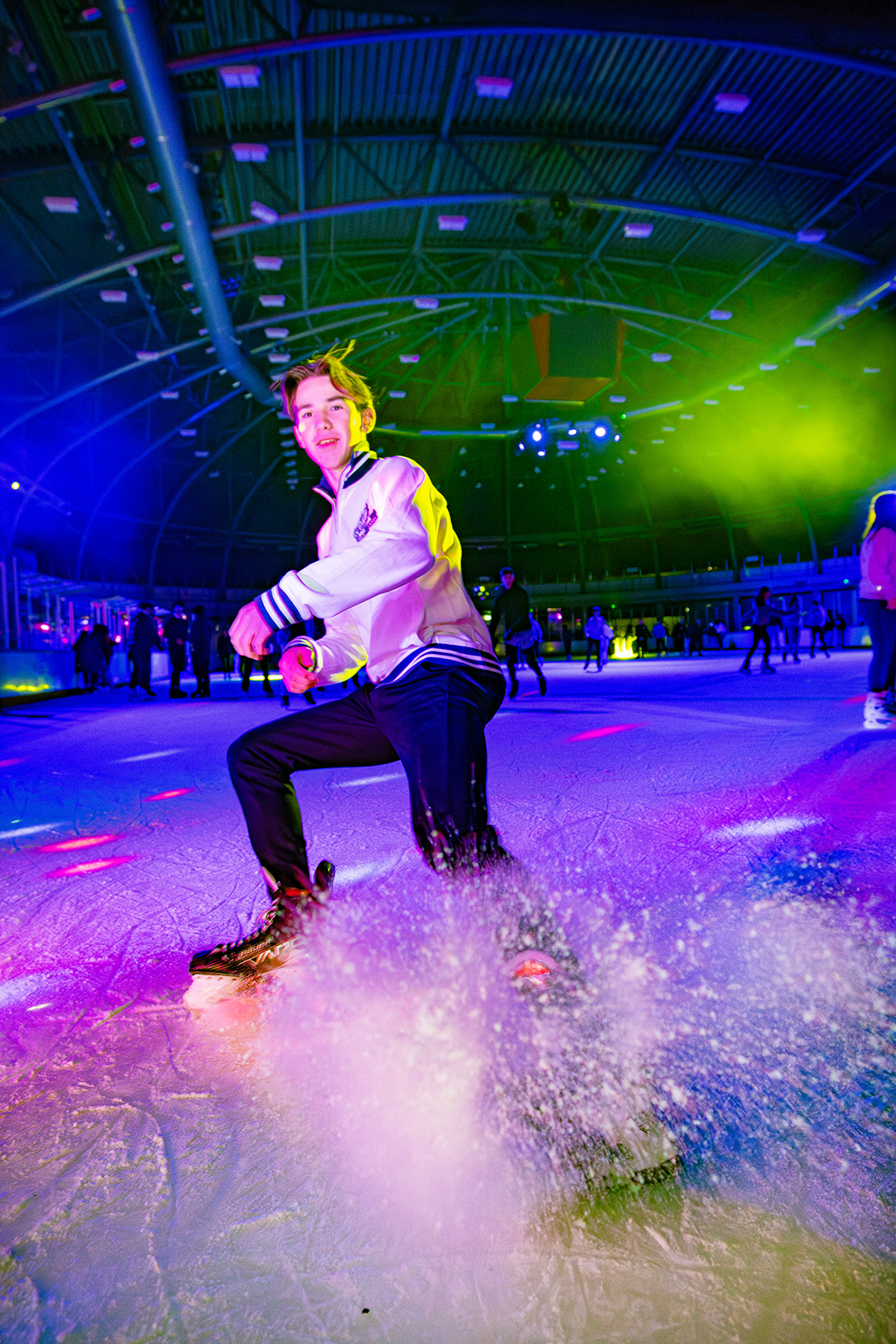 Een jongen schaatst en remt net voor de camera waardoor er allemaal ijs opspat tijdens het disco schaatsen.