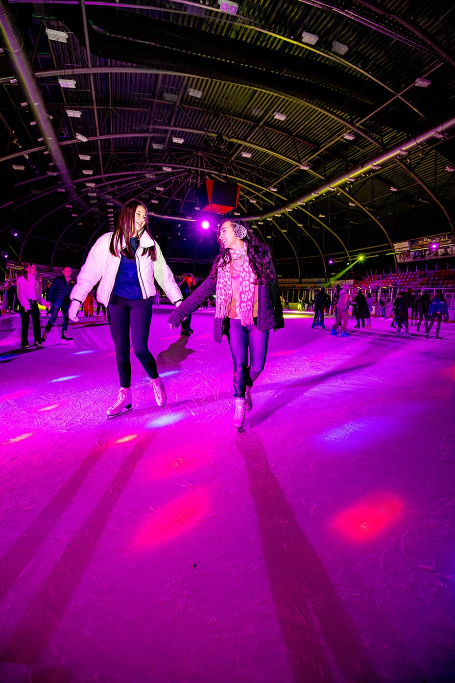 Twee dames schaatsen hand in hand tijdens het disco schaatsen.
