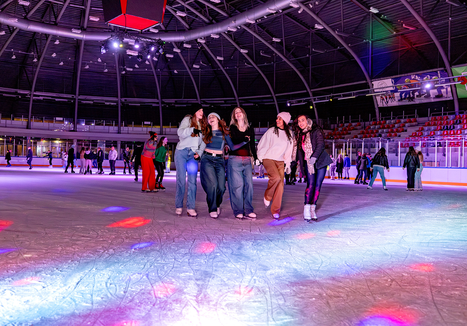 Vijf meiden naast elkaar lachend op het ijs tijdens disco schaatsen.