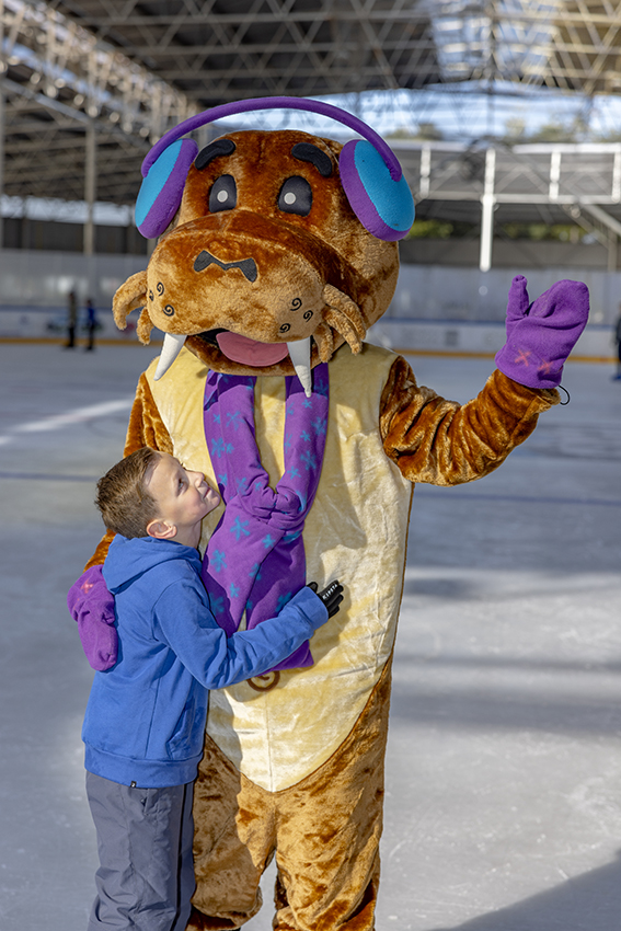 Een jongen knuffelt mascotte Wus tijdens het recreatief schaatsen bij een Optisport schaatsbaan.