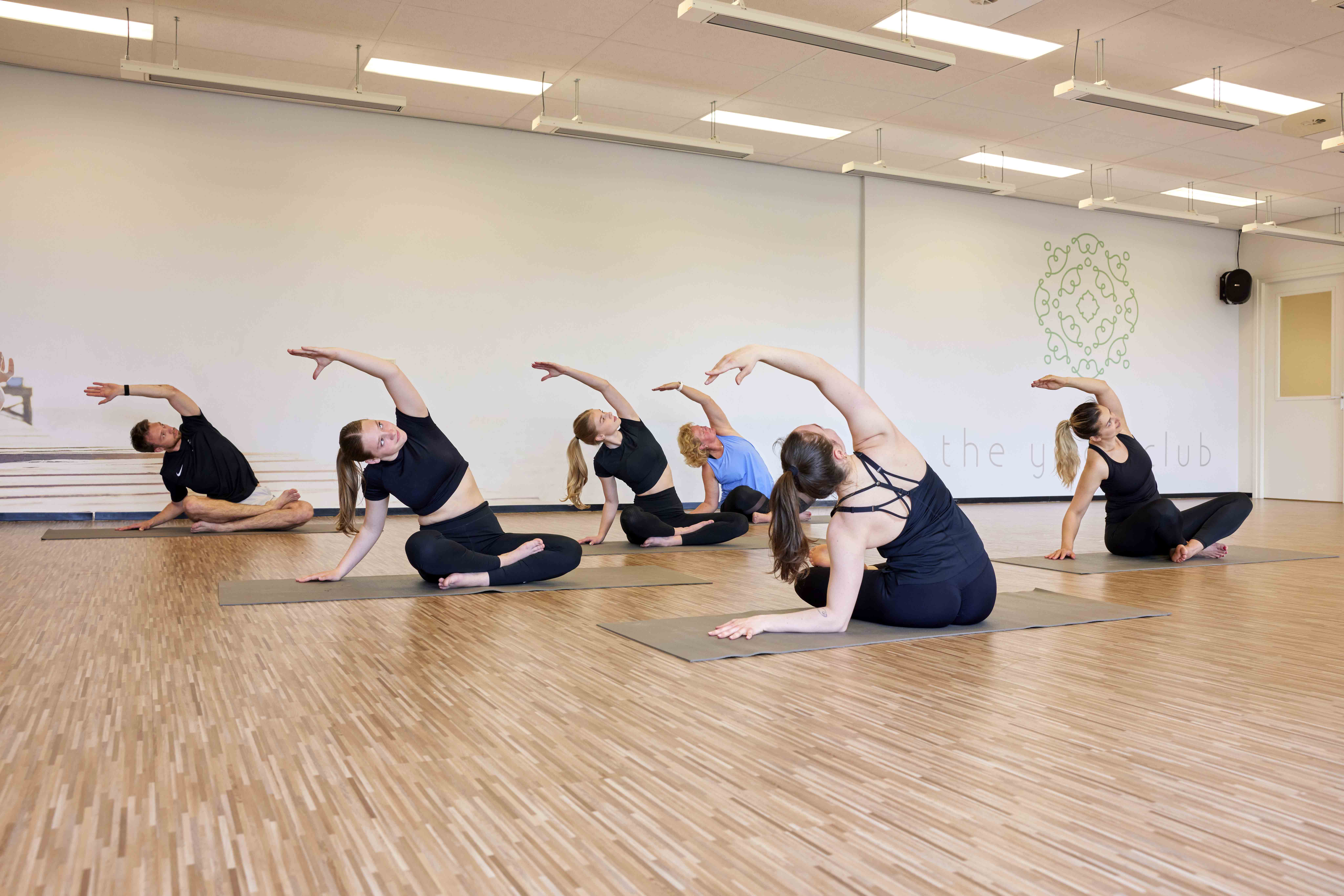 Groep mensen zit op yoga matje met arm in de lucht