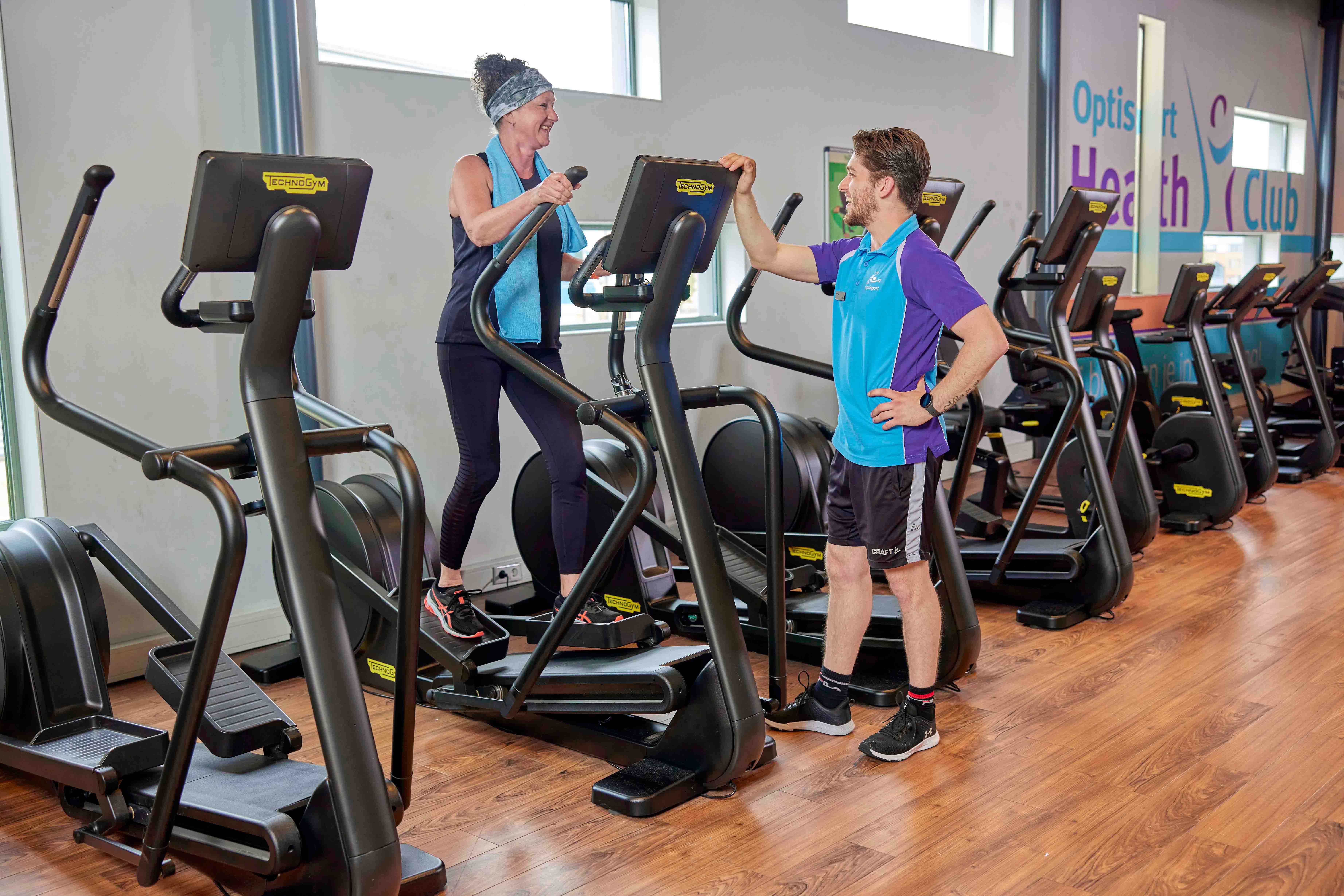 Een vrouw doet oefeningen onder begeleiding van een instructeur tijdens een groepsles Cardio fitness van Optisport.