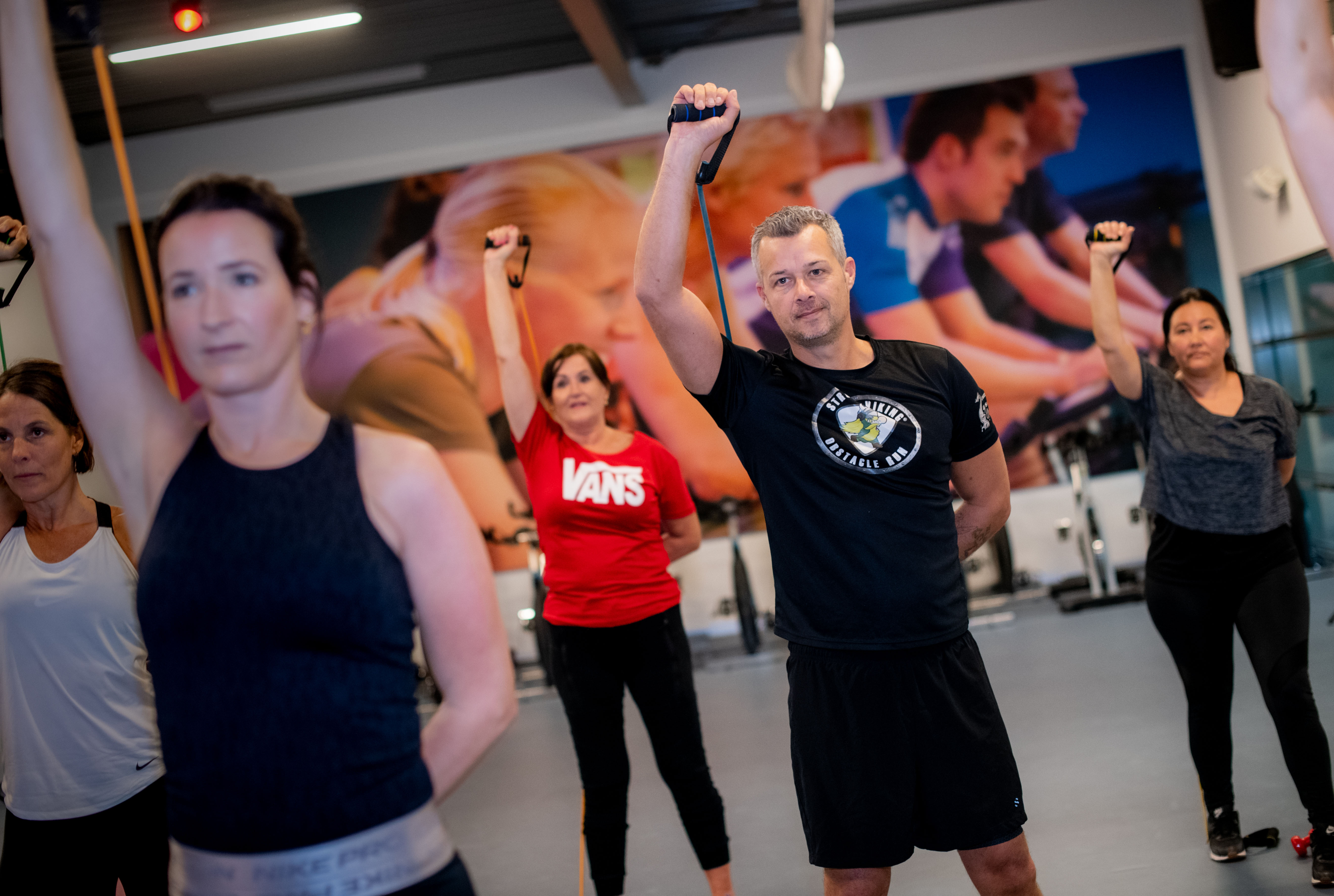 ClubFitShape bij Optisport. Een groep mannen en vrouwen doen oefeningen tijdens de groepsles met plezier onder begeleiding van een instructeur van Optisport.