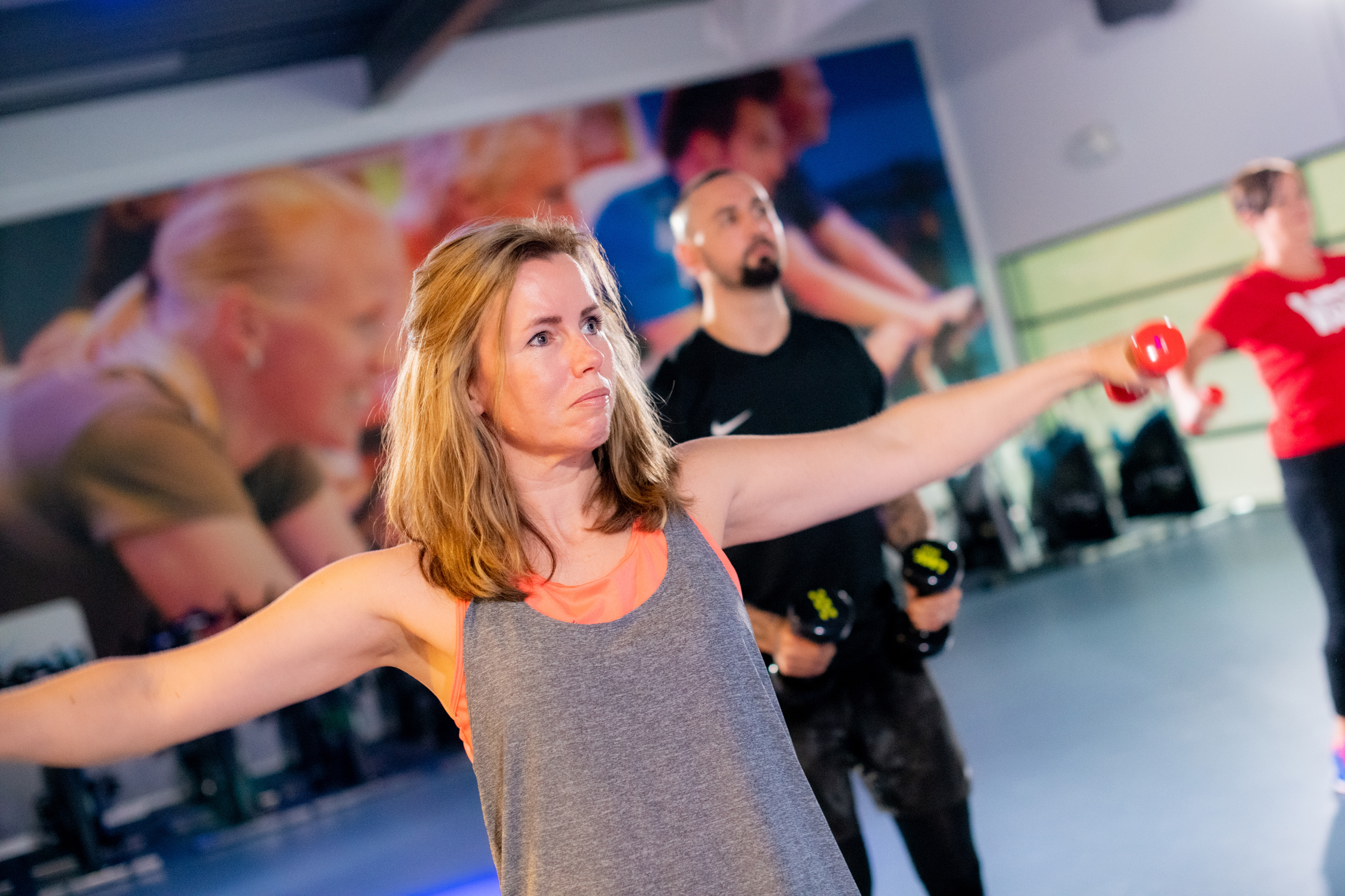 ClubFitShape bij Optisport. Een groep mannen en vrouwen doen oefeningen tijdens de groepsles met plezier onder begeleiding van een instructeur van Optisport.