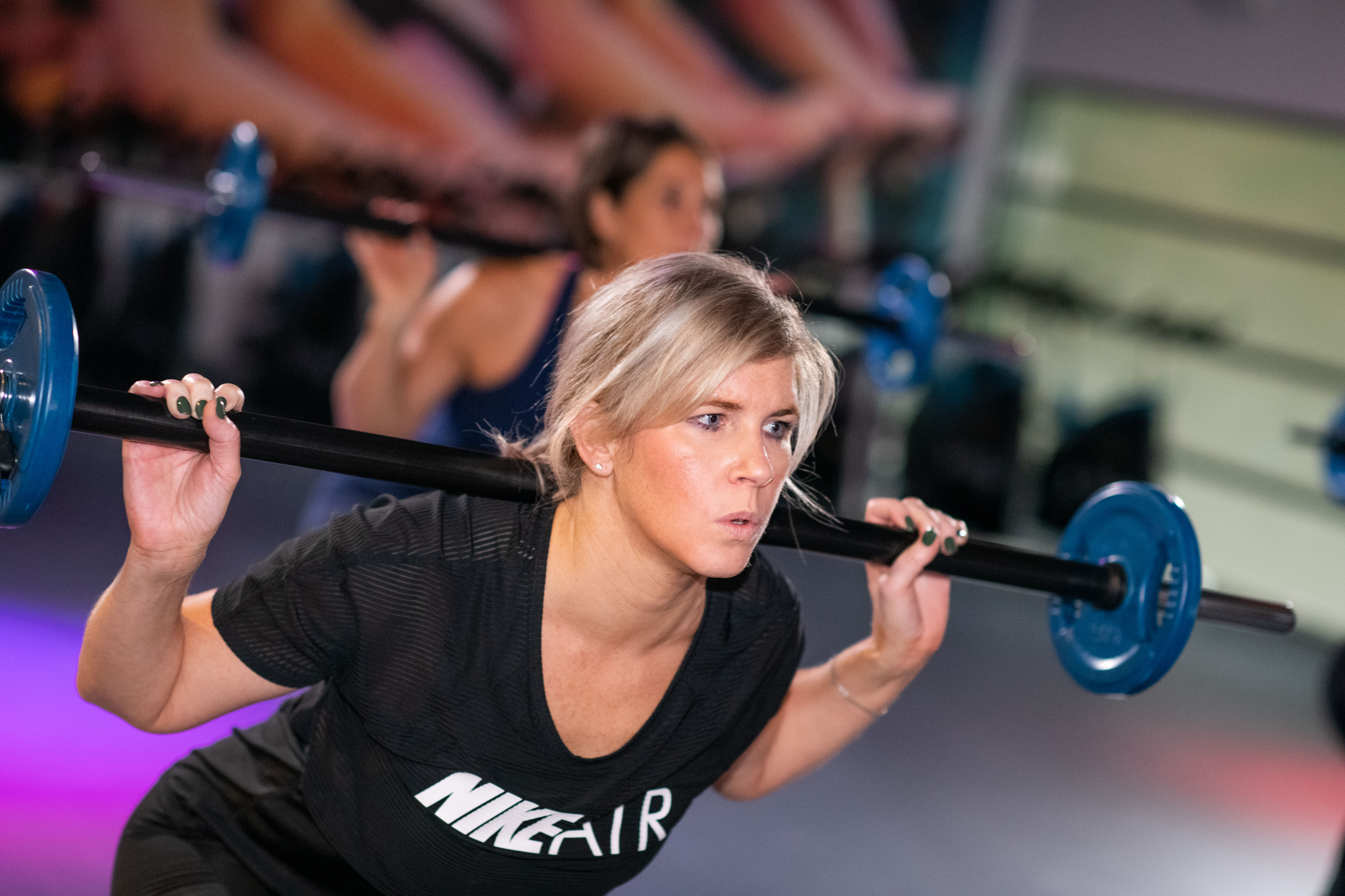 Vrouw doet squats met stang in haar nek tijdens les Combifit