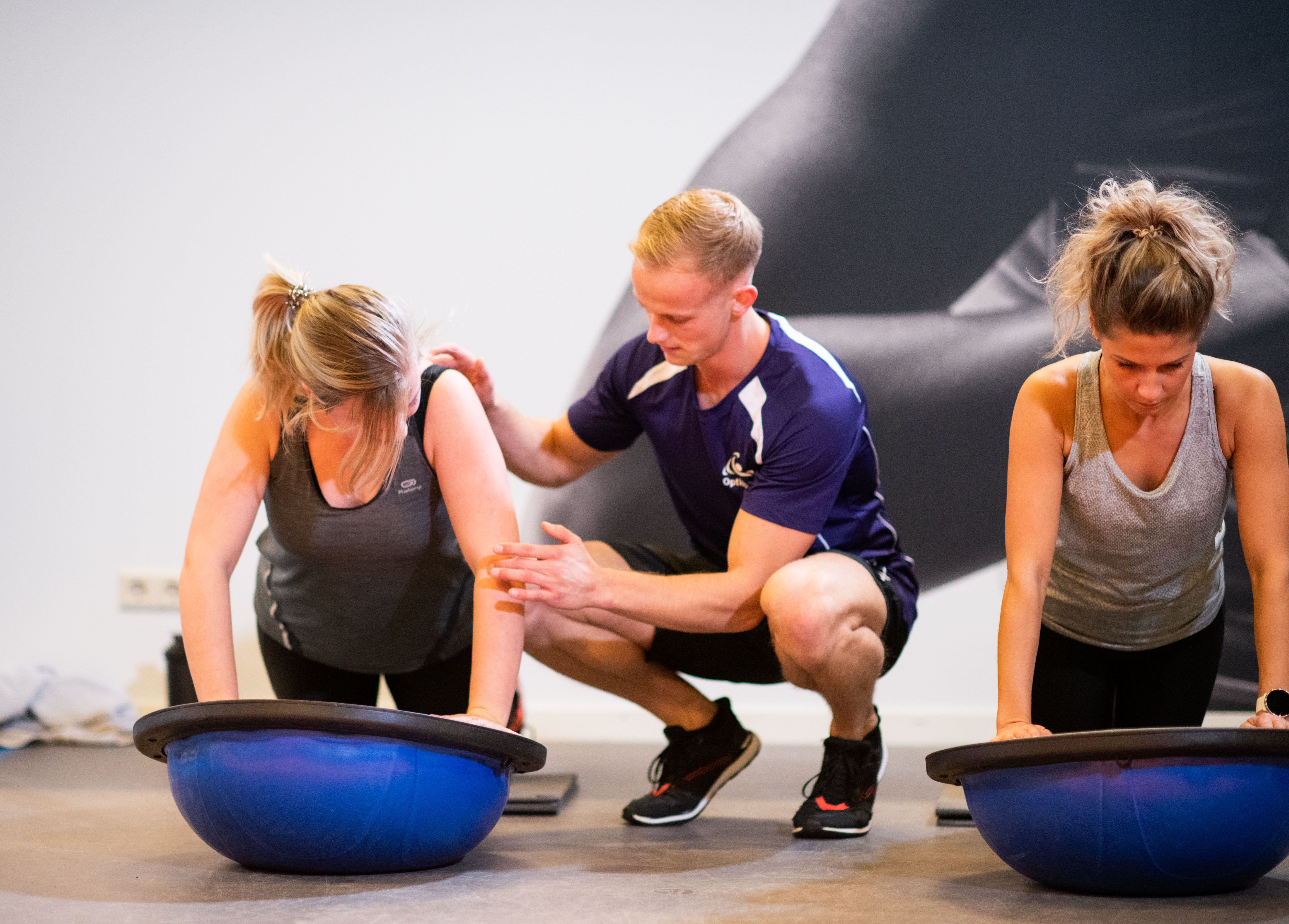 Twee vrouwen balanceren met de armen op een halve yogabal en krijgen instructies van instructeur 