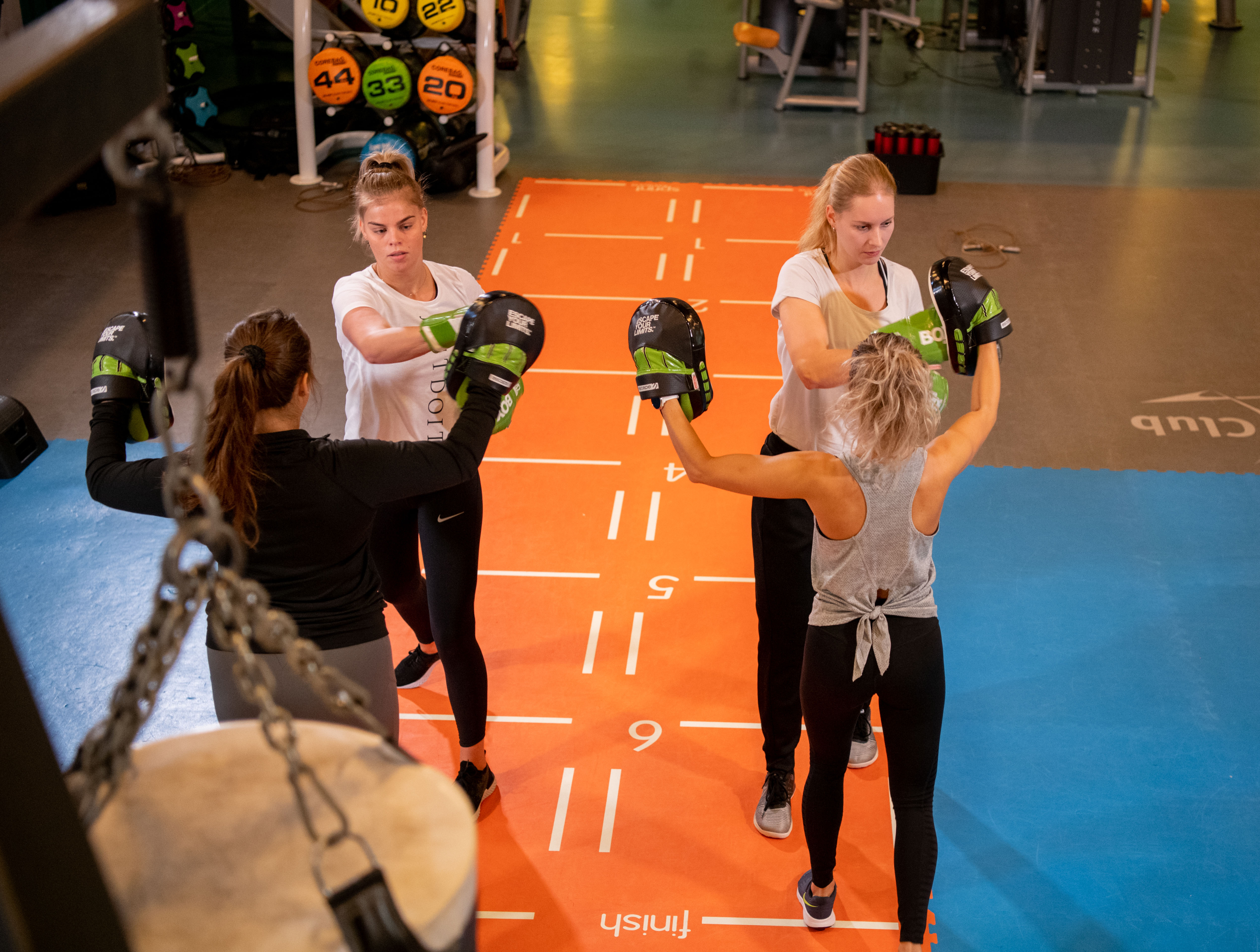 Twee vrouwen zijn aan het boksen zonder lichamelijk contact. Ze doet oefeningen met plezier onder begeleiding van een instructeur van Optisport.