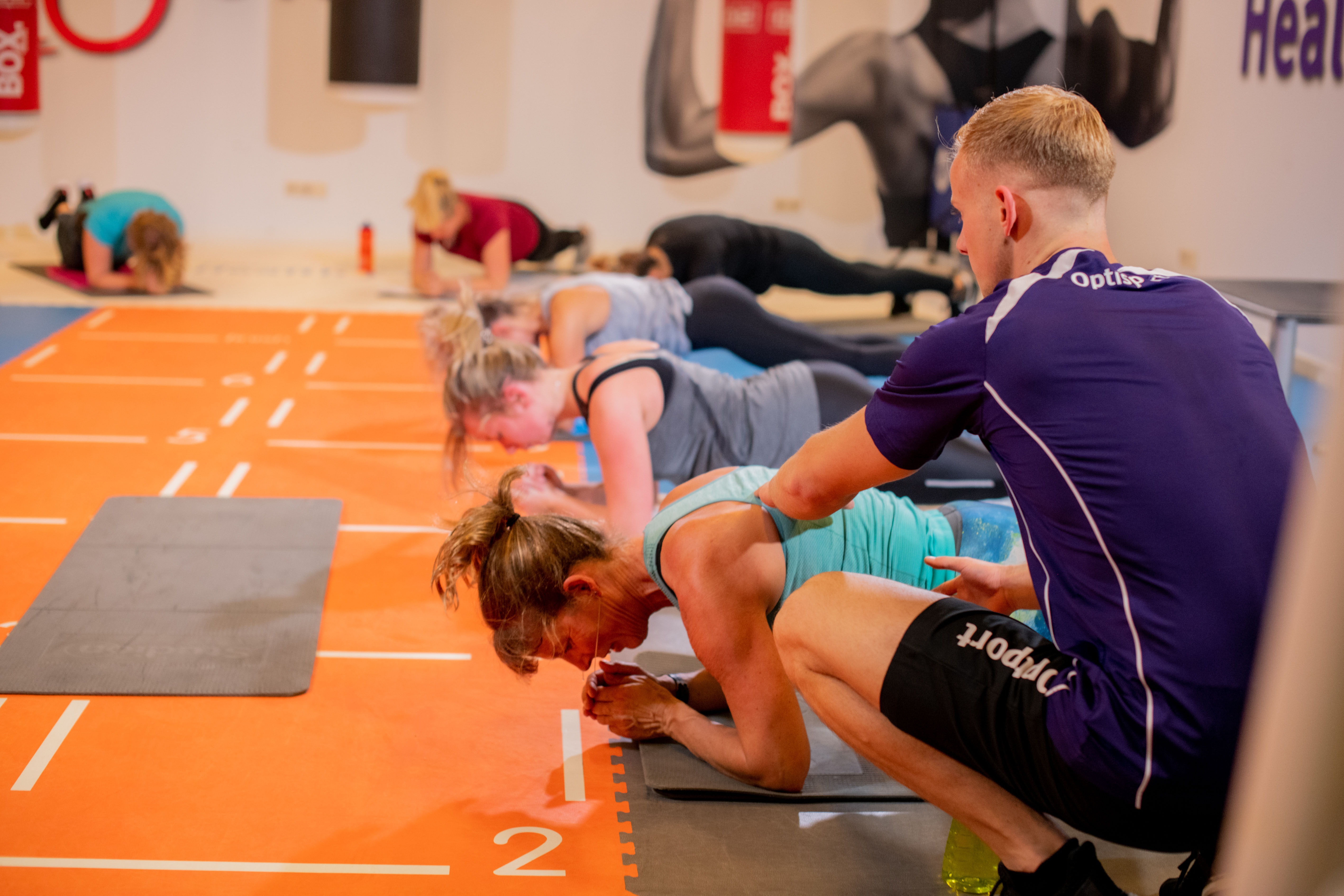 Een groep mensen zijn oefeningen aan het doen bij een Optisport locatie onder begeleiding van een instructeur.