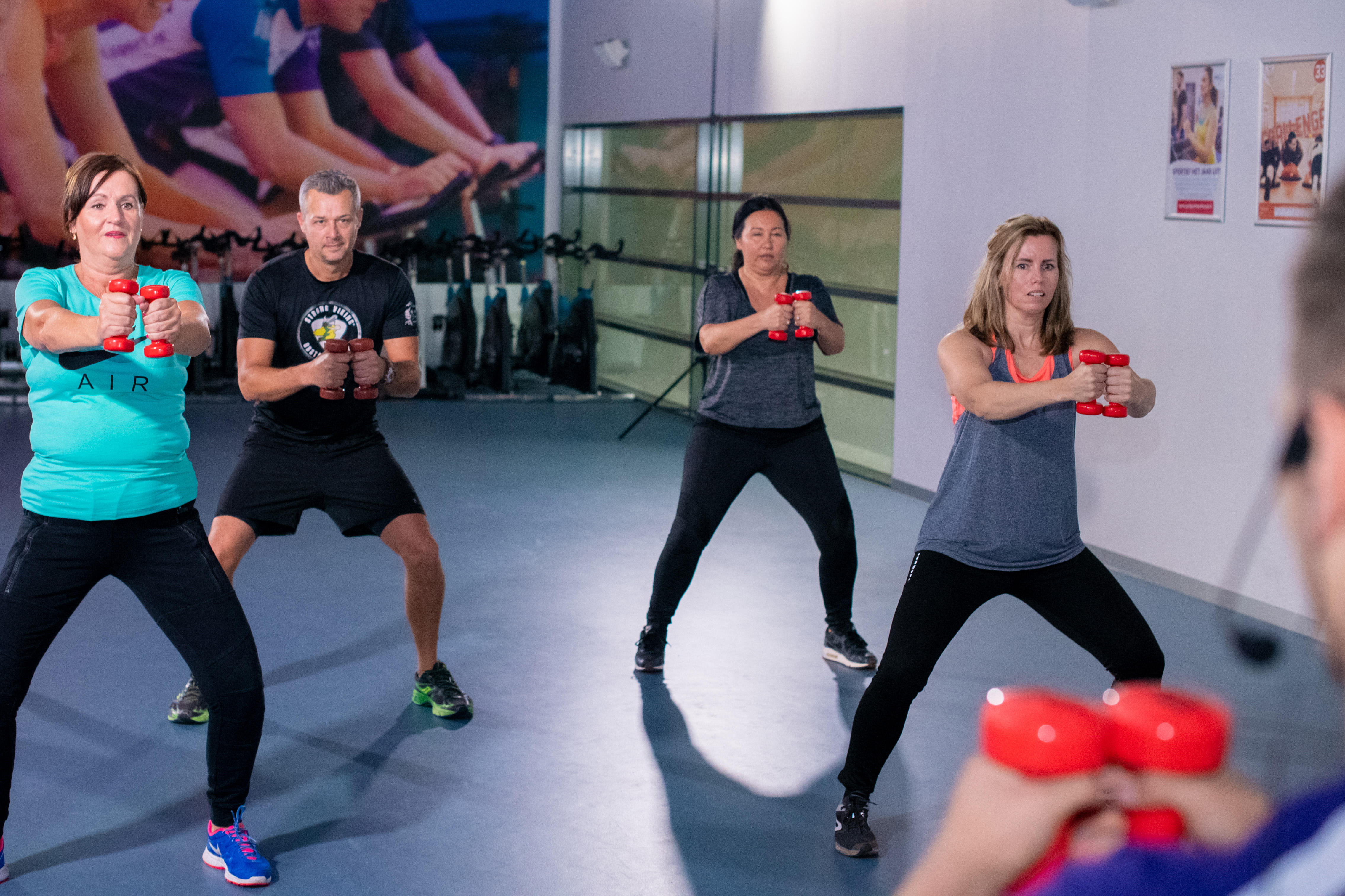 Workout voor vijftigplussers gericht op conditie, kracht en lenigheid. Groep mensen doen verschillende oefeningen.