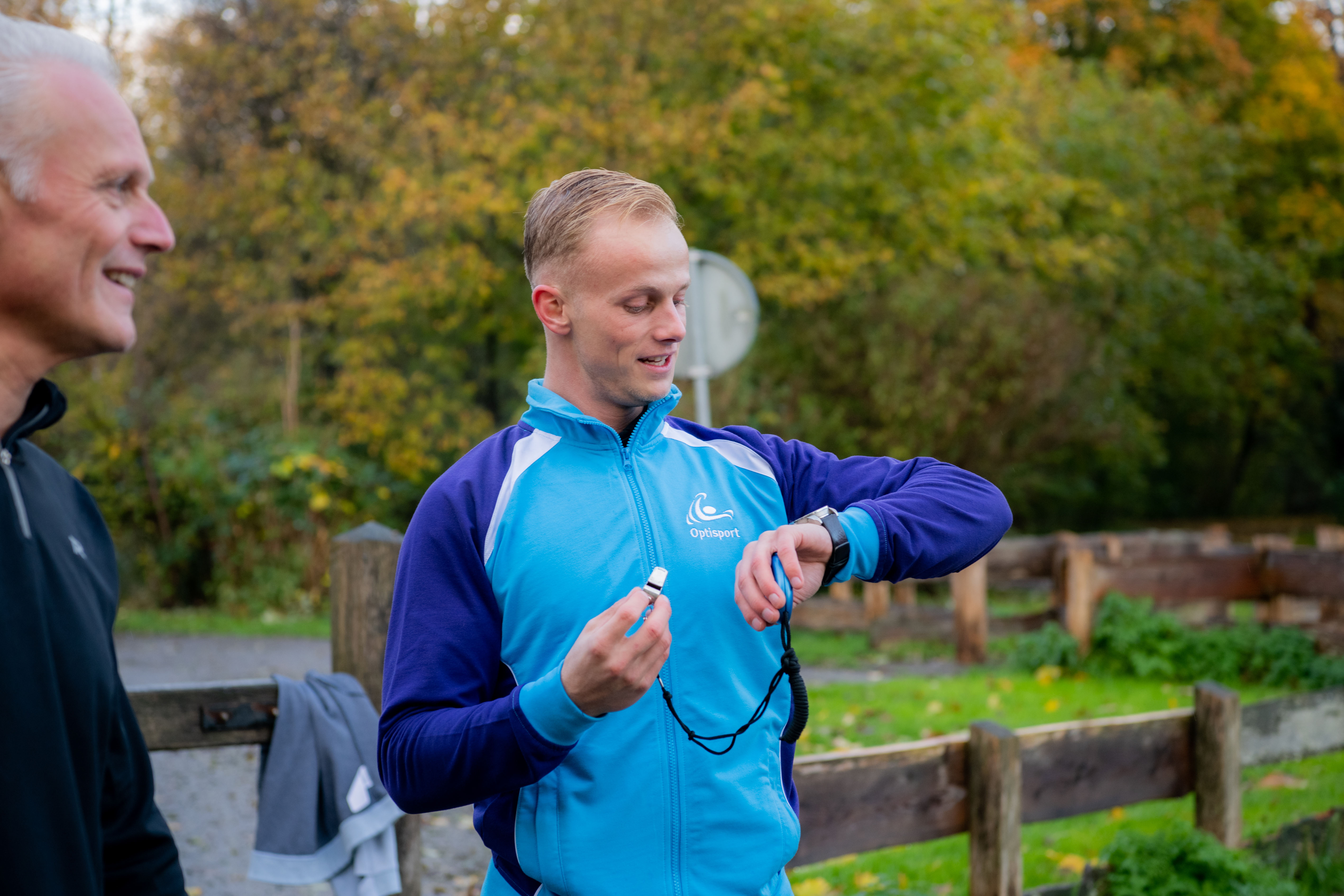 Trainer van de Hardlooptraining kijkt op zijn horloge en wilt op zijn fluitje blazen