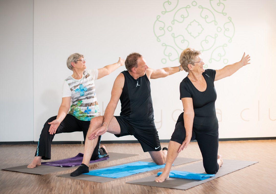 Twee vrouwen en een man doen oefening tijdens Flow Yoga