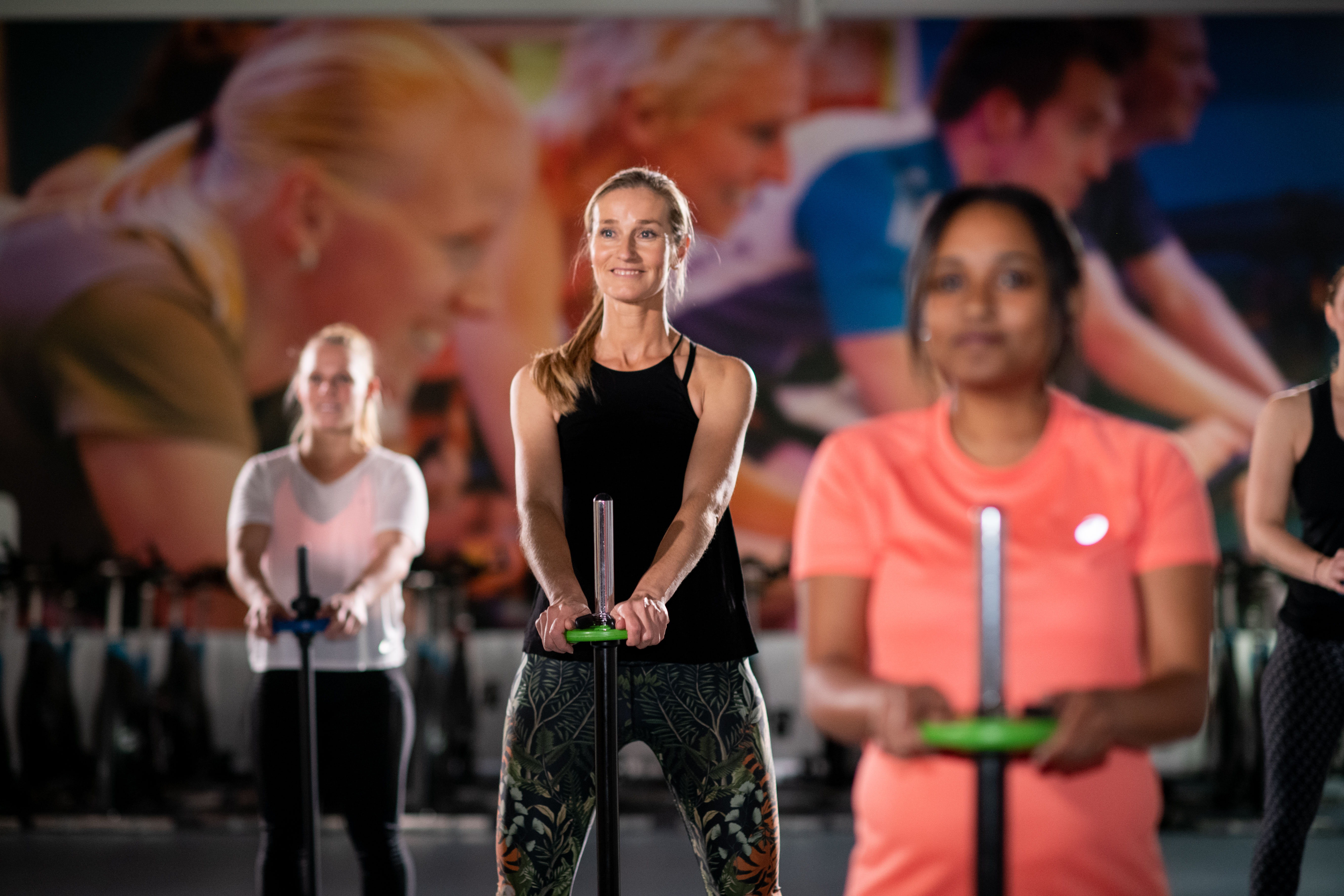 Drie vrouwen doen oefening met stang verticaal.