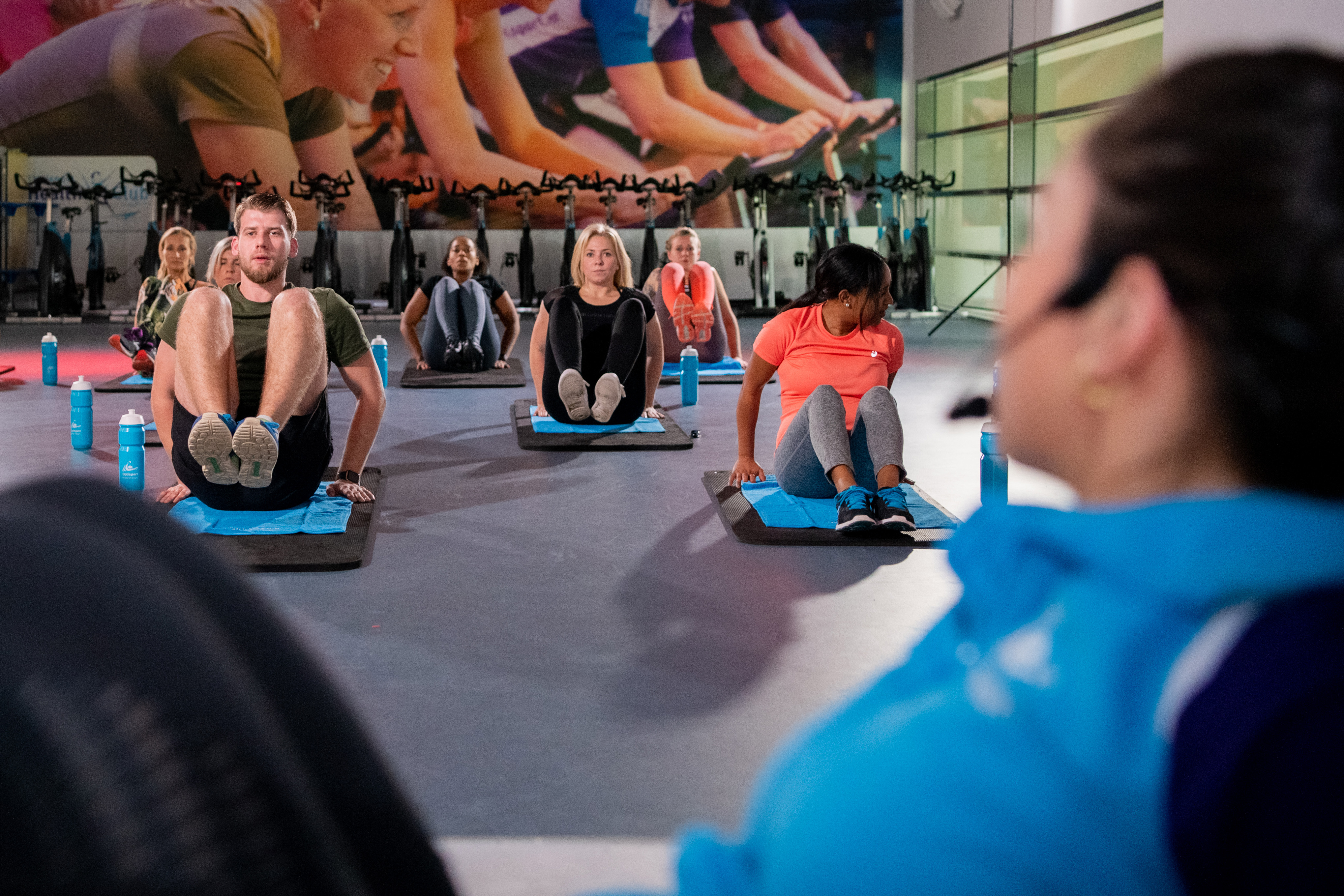 Groep mensen zit op yogamatje met de benen van de grond getild