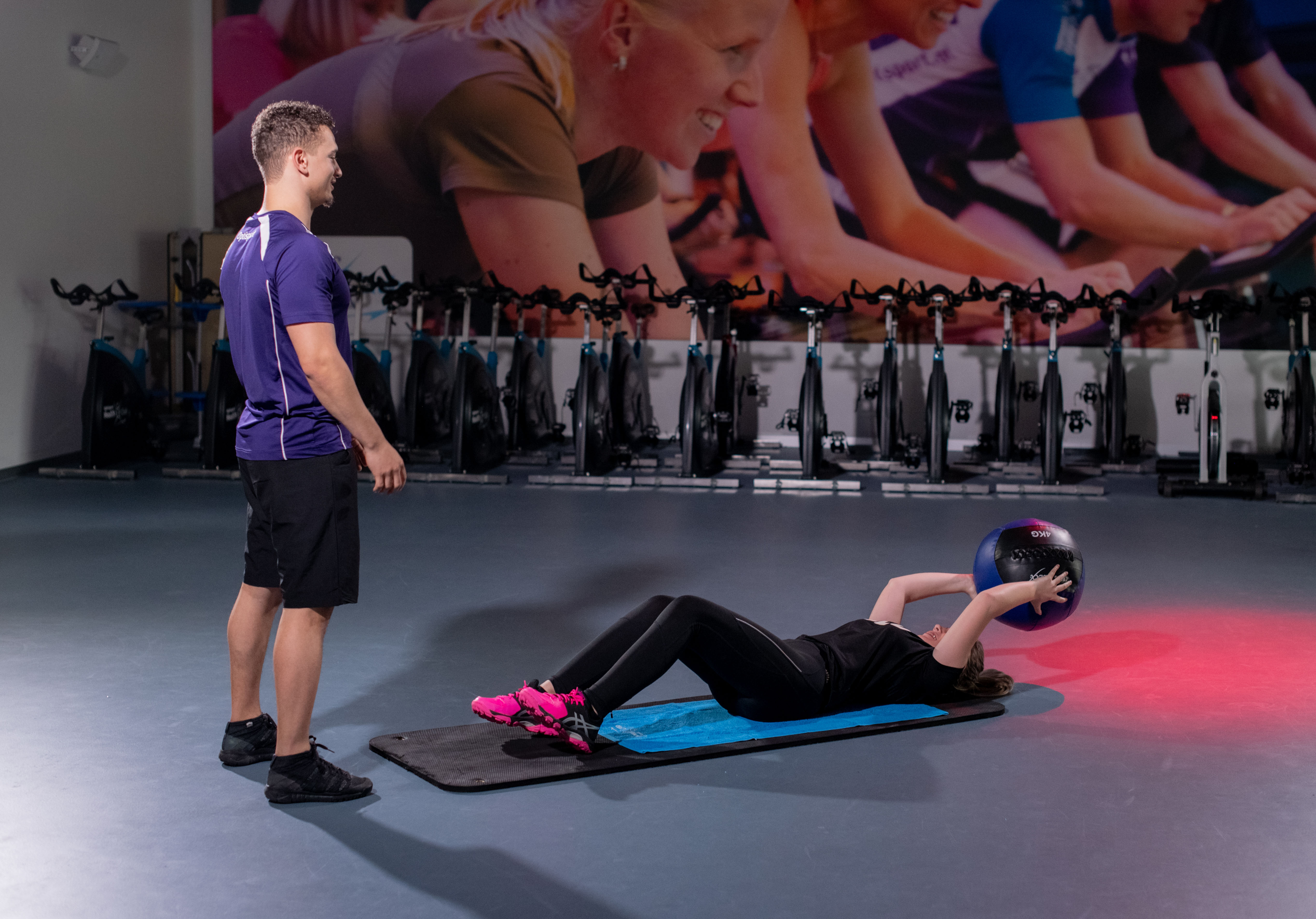 Meisje ligt op haar rug en doet oefening met medicine bal tijdens de jeugdfitness. Instructeur staat voor haar