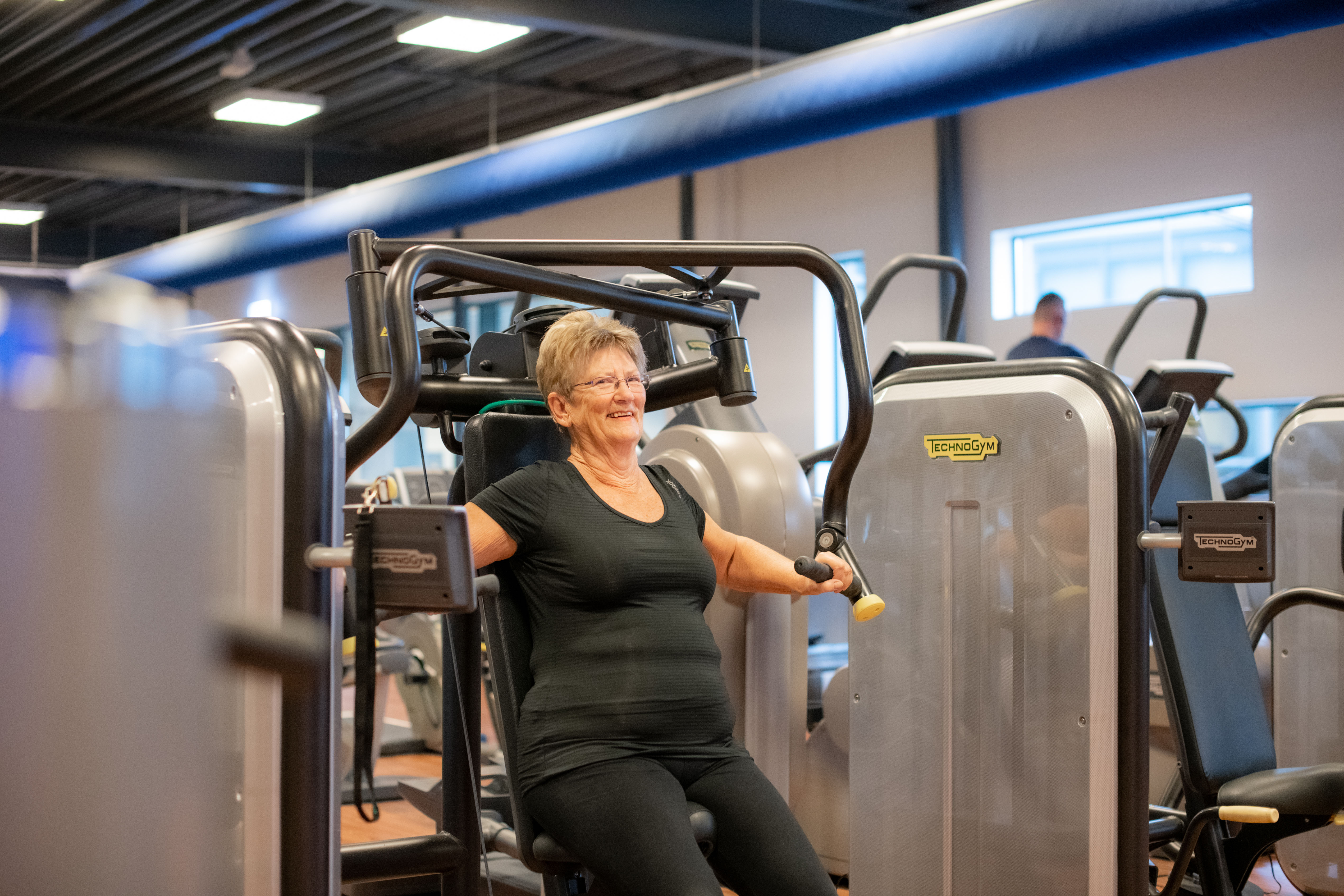 Fitness bij Optisport. Seniorenfitness, een vrouw is oefeningen aan het doen onder begeleiding van een instructeur.