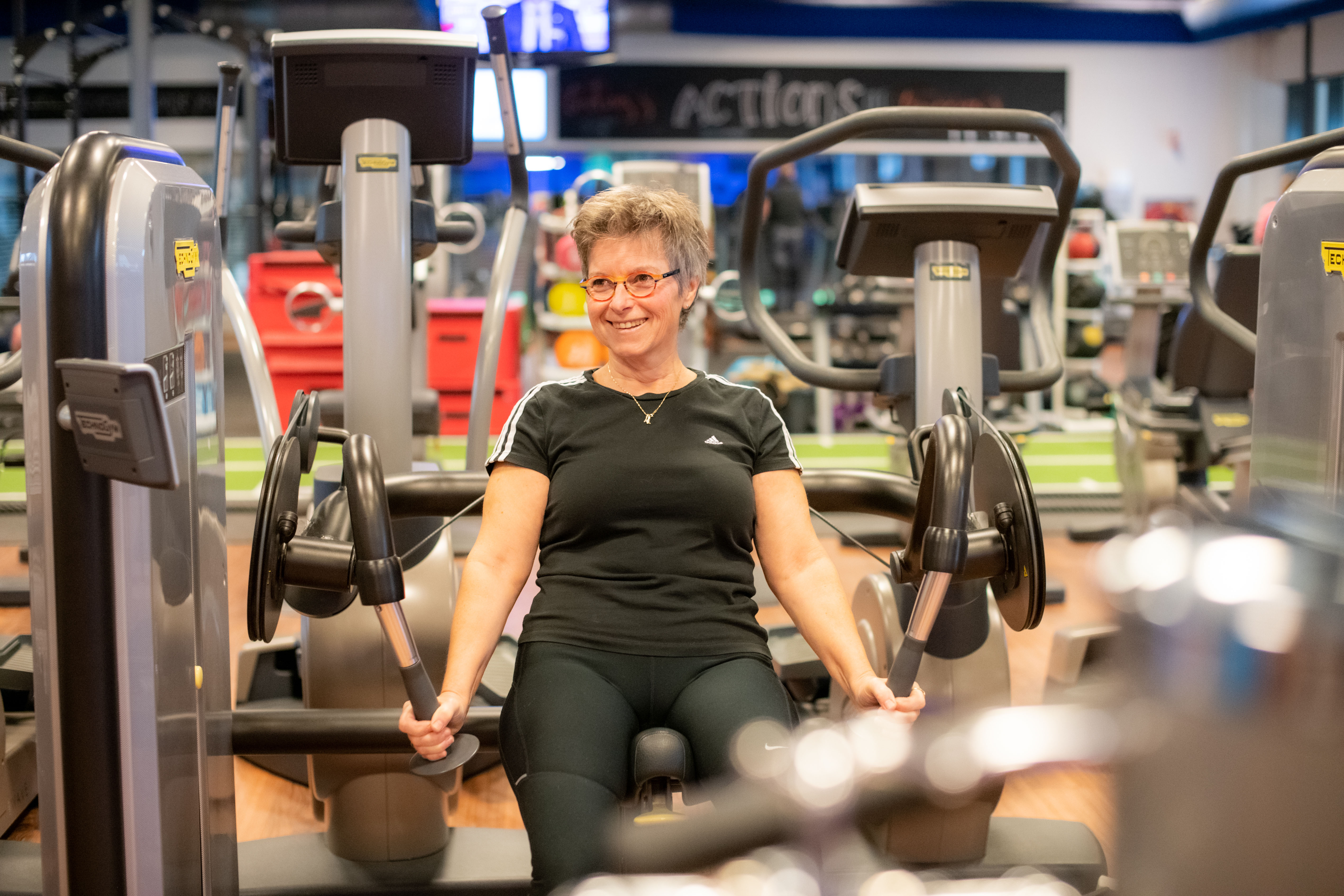 Fitness bij Optisport. Seniorenfitness, een vrouw is oefeningen aan het doen onder begeleiding van een instructeur.