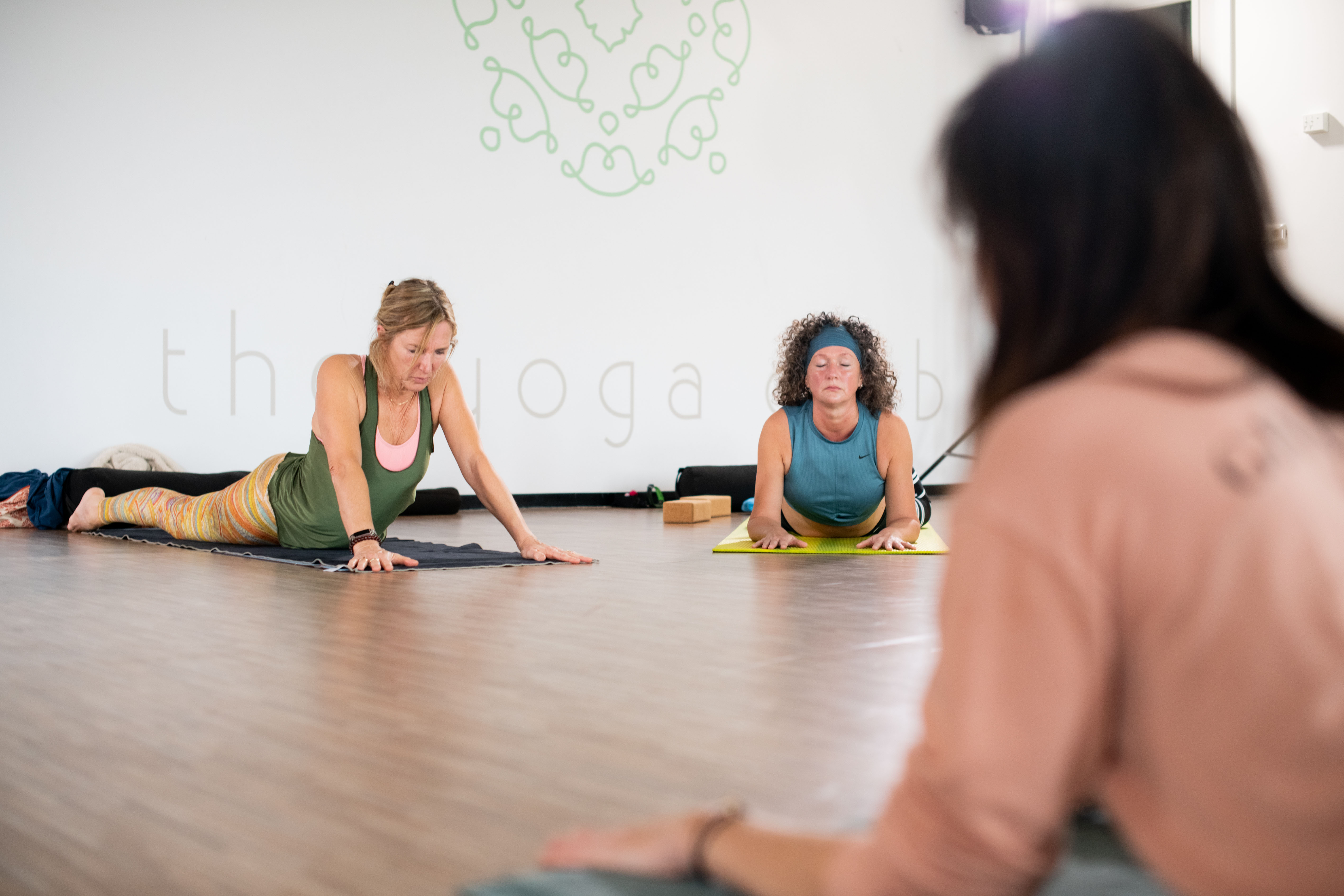 Twee vrouwen doen yoga oefeningen onder toeziend oog van een instructeur.