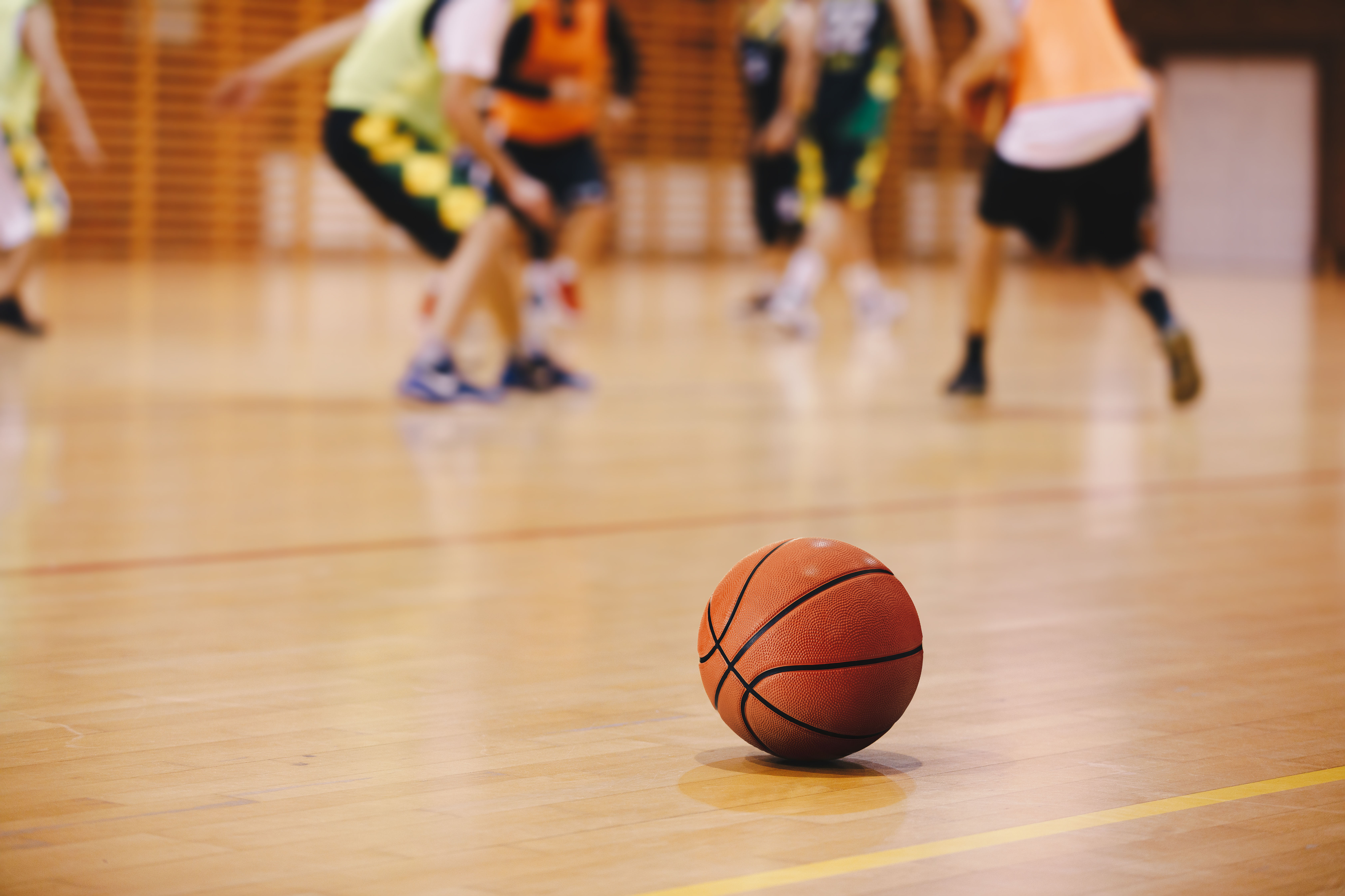 Er ligt een basketbal op de grond, terwijl kinderen op de achtergrond aan het spelen zijn.