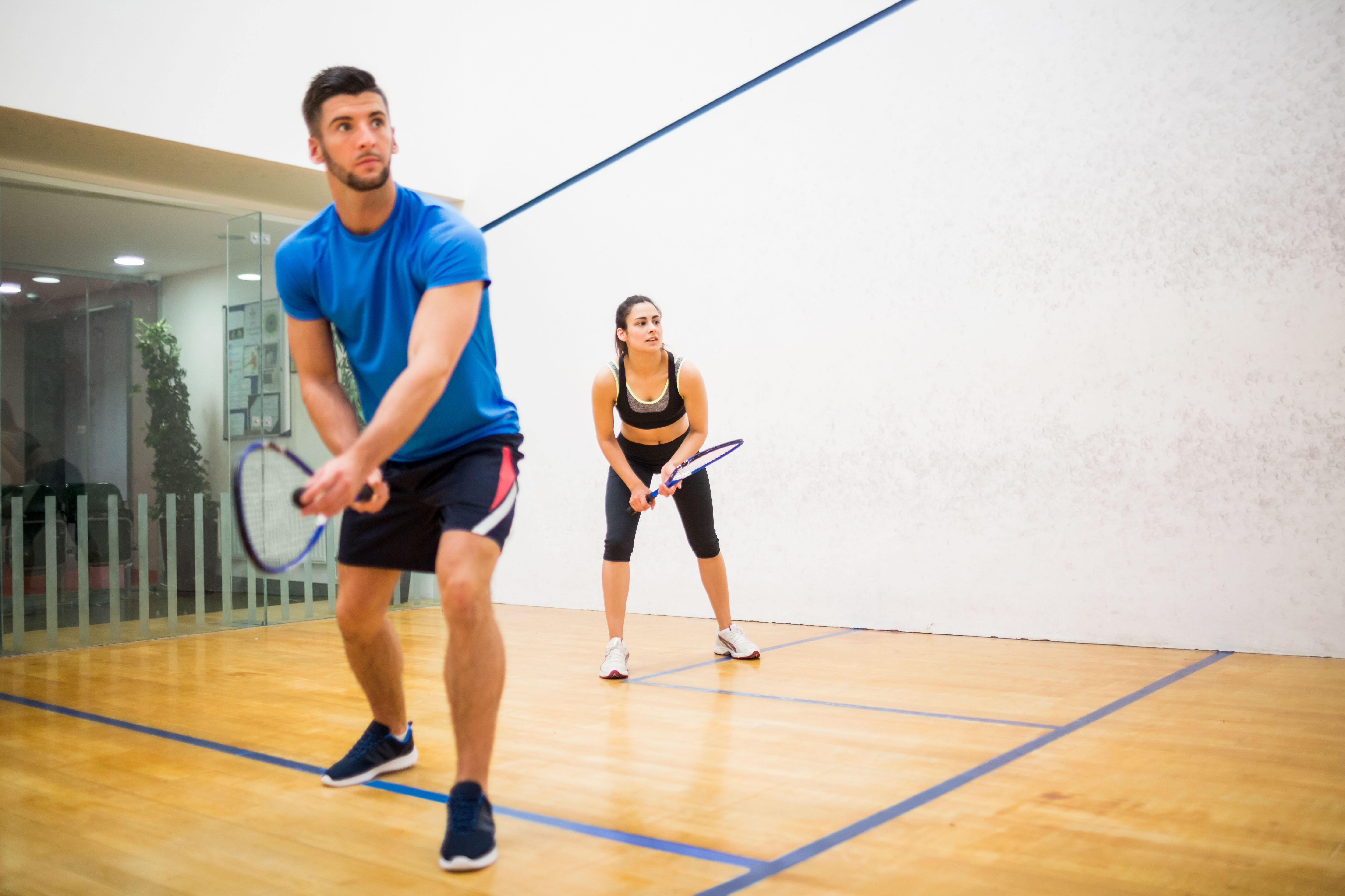 Squashen bij Optisport. Man en vrouw spelen squash en zijn dit met veel plezier aan het doen.