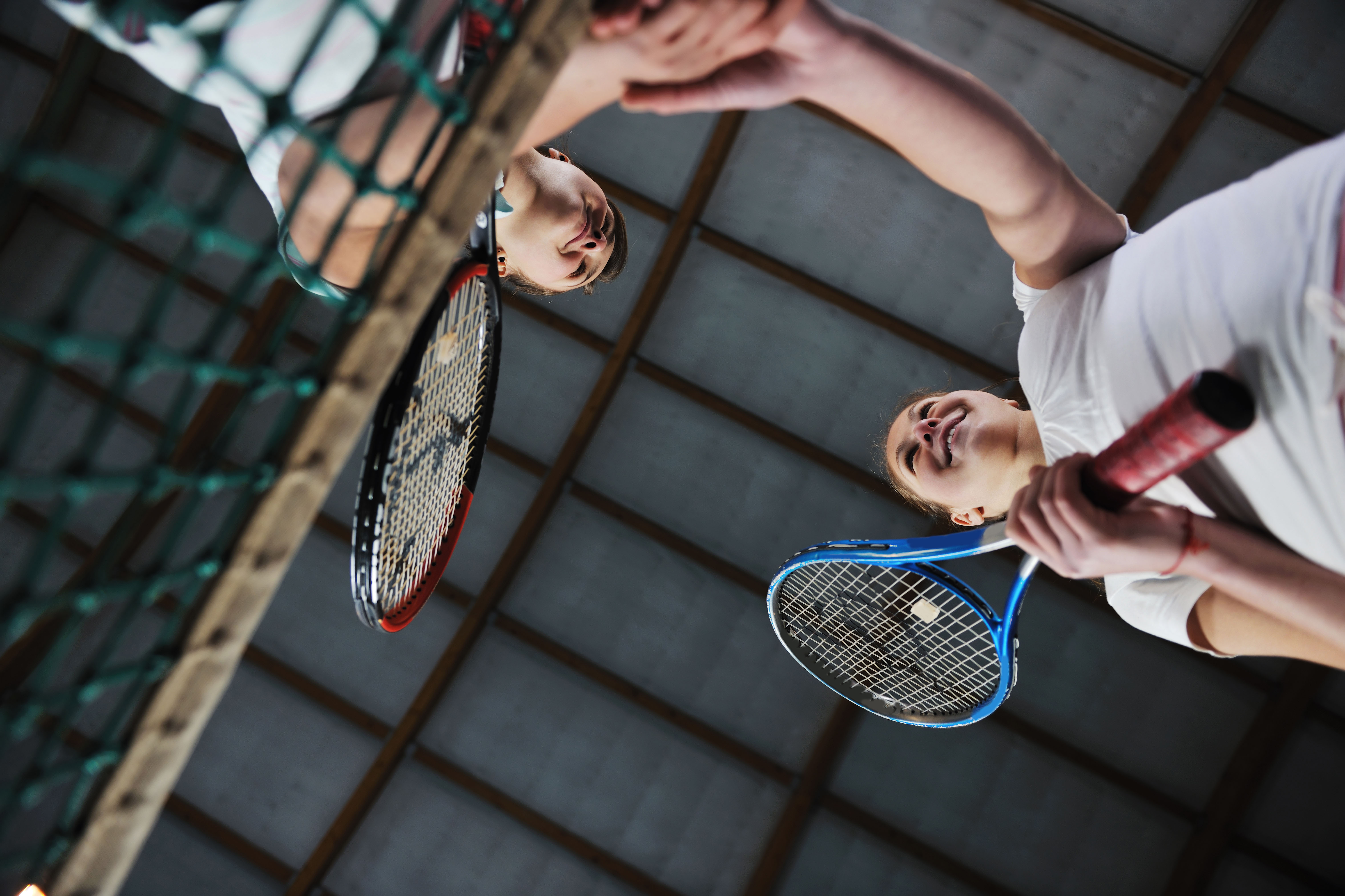 Twee mensen staat bij het net op een tennisbaan en geven elkaar een hand.