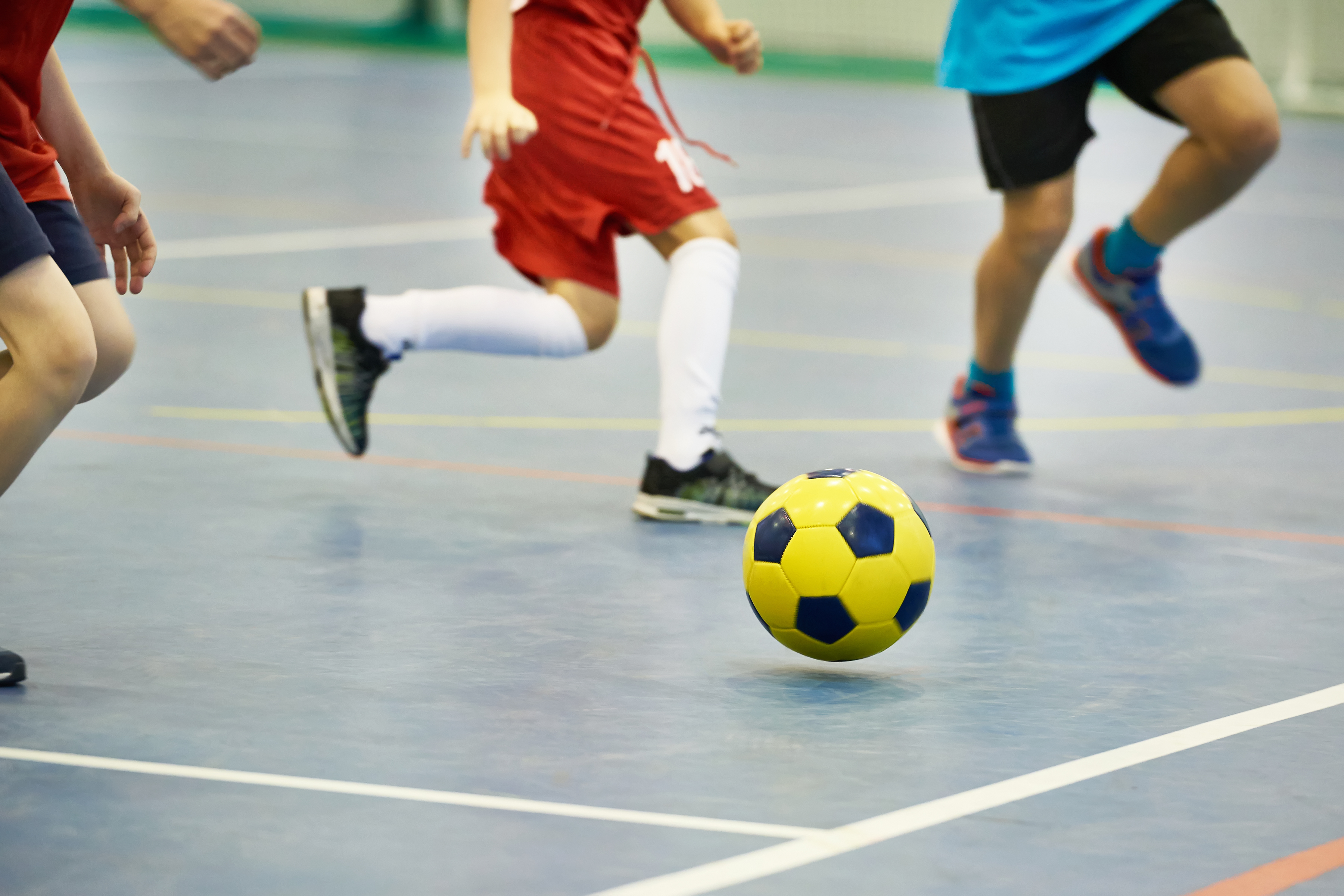 Kinderen rennen achter een bal aan in een sporthal tijdens het voetballen.