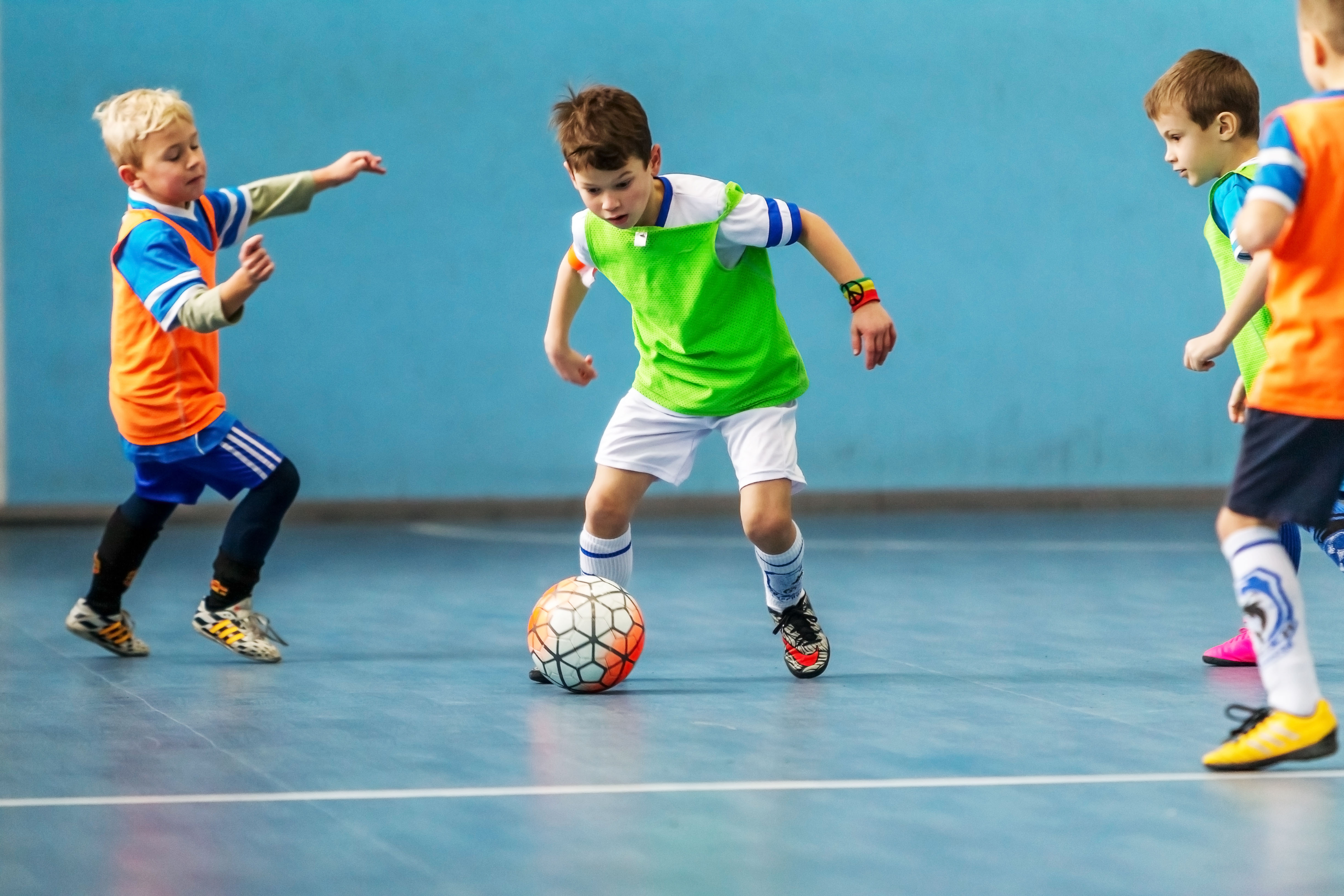 Zeskamp bij Optisport De Kreek. Een groep jongens is aan het voetballen in de zaal en hebben plezier.