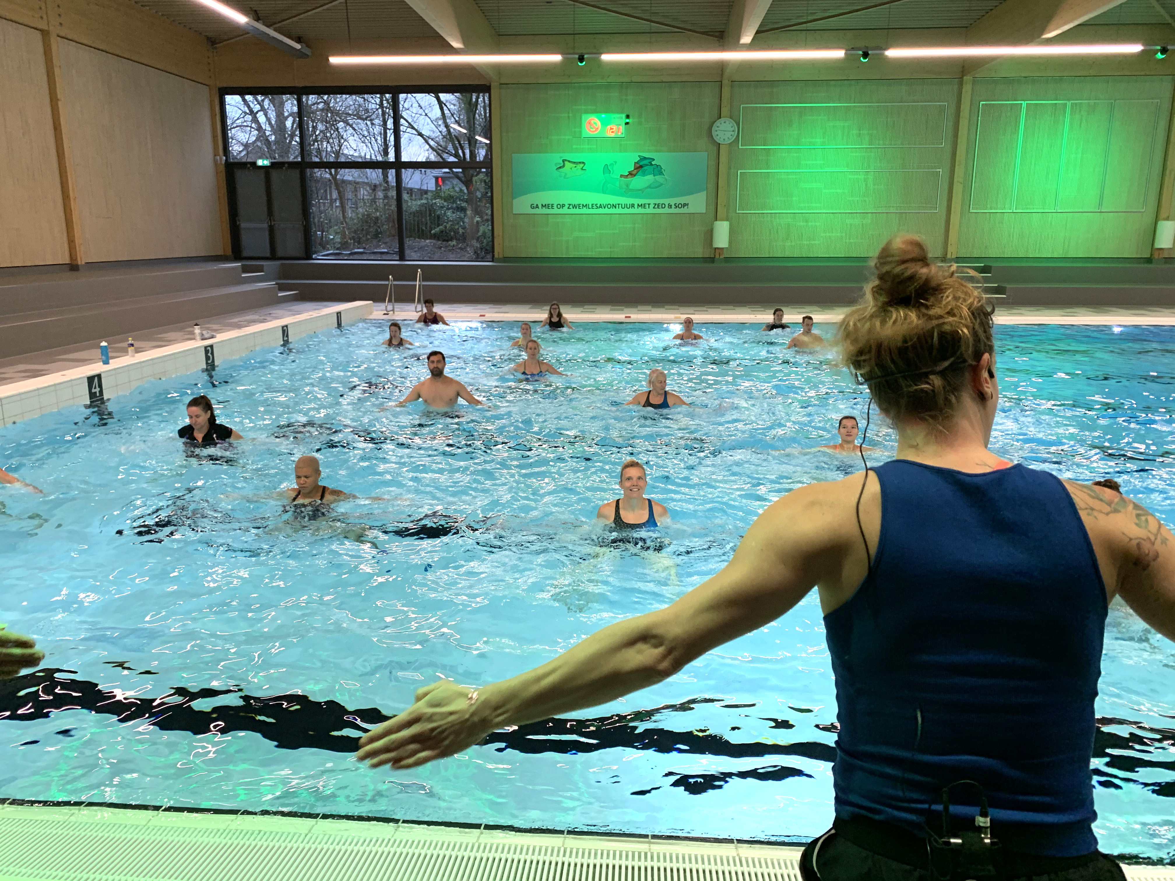 Instructeur doet oefeningen voor die groep mensen in zwembad na doet