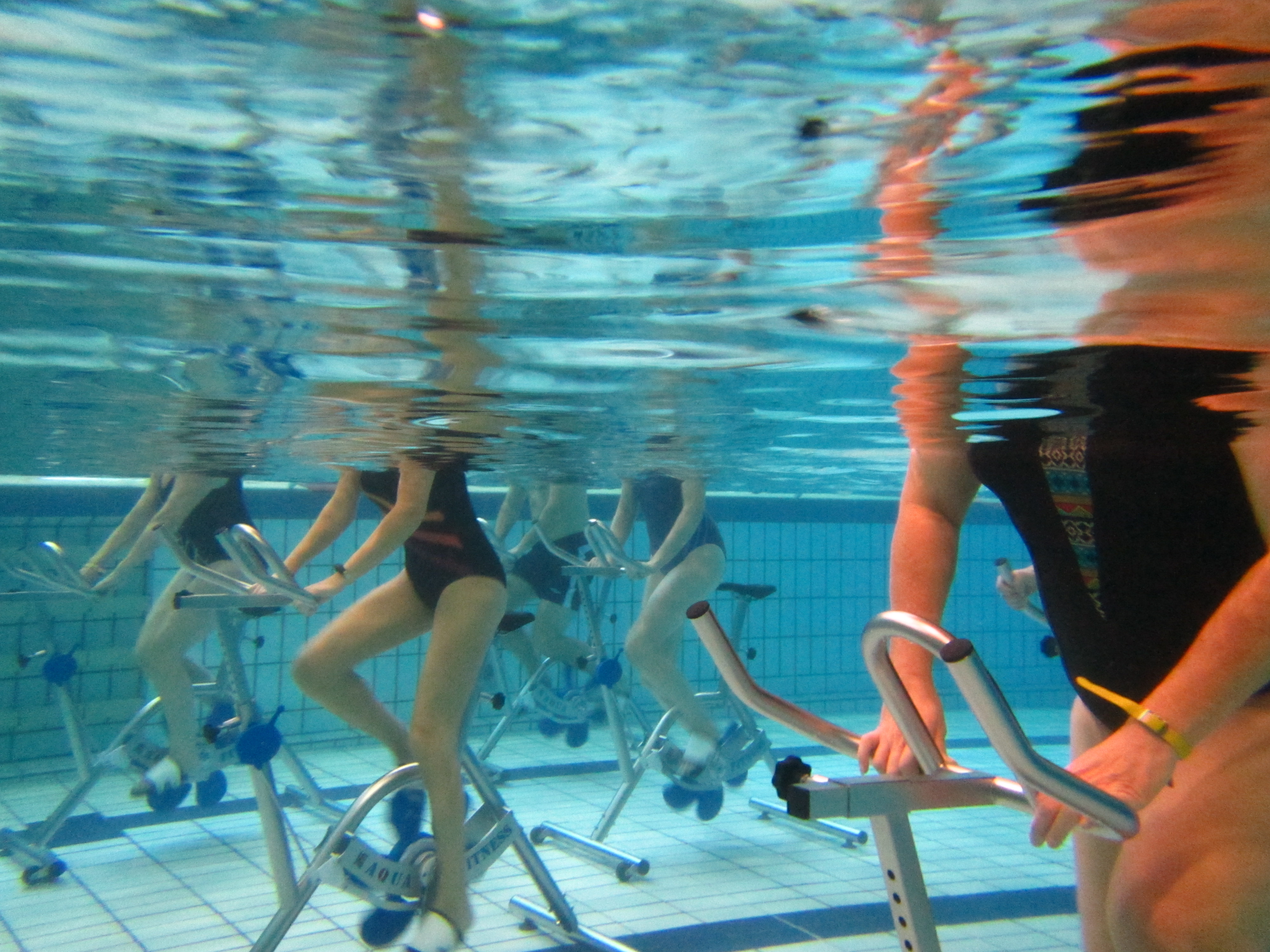Deelnemers fietsen onderwater en doen aquaspinning oefeningen tijdens een les Aqua'Spinning bij Optisport.