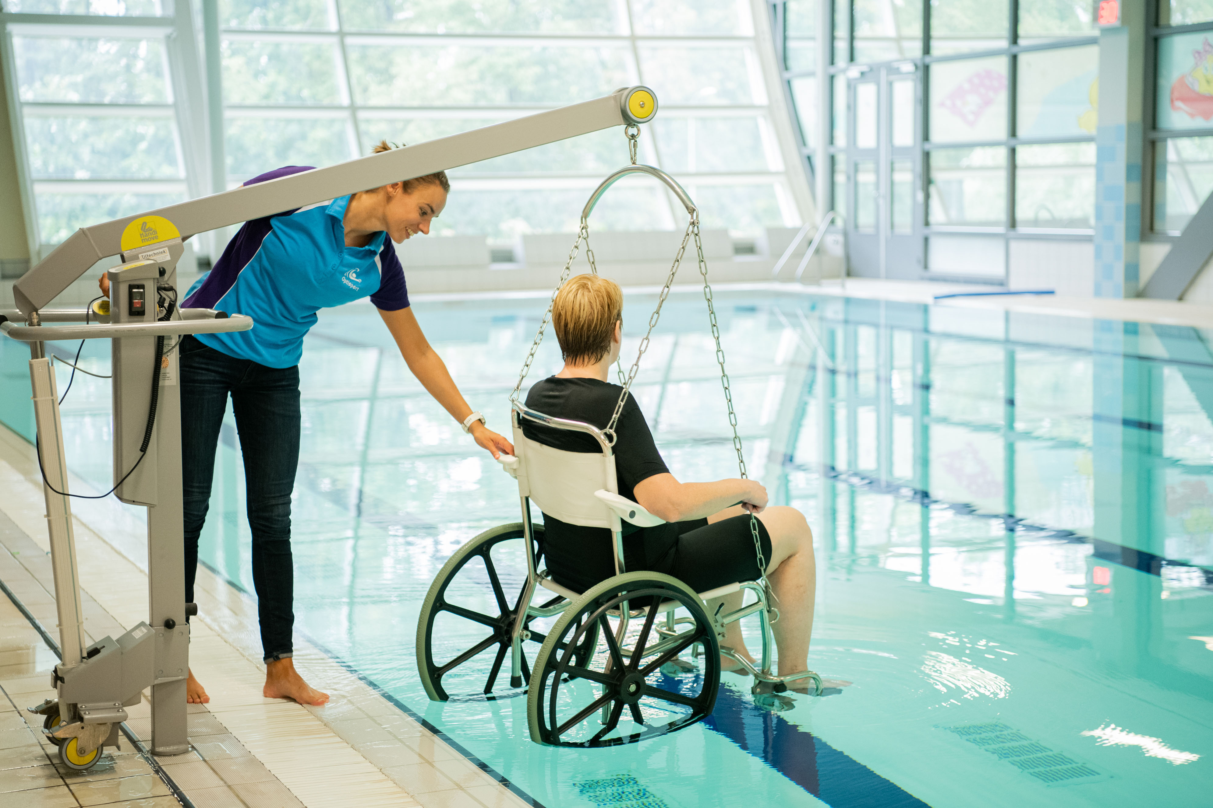 Vrouw in rolstoel hangt boven het water met instructrice naast haar