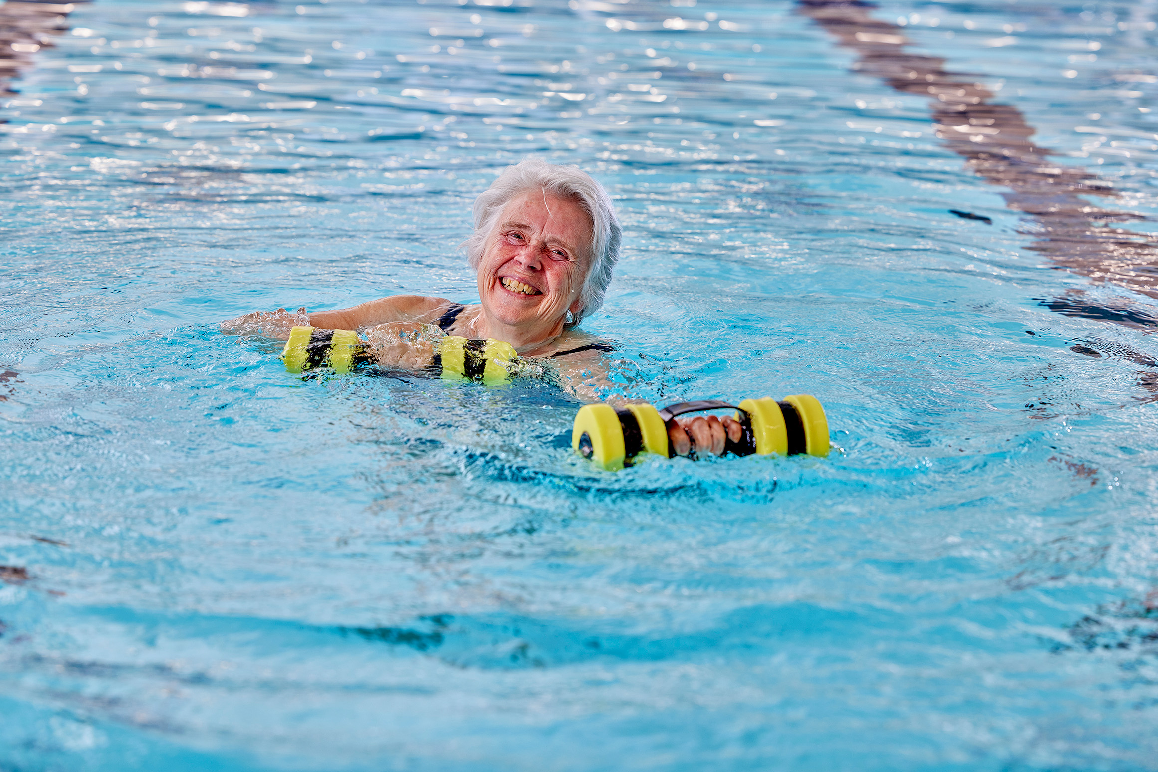Oudere dame traint met gewichten in het zwembad van Optisport tijdens een AquaVitaal groepsles. 