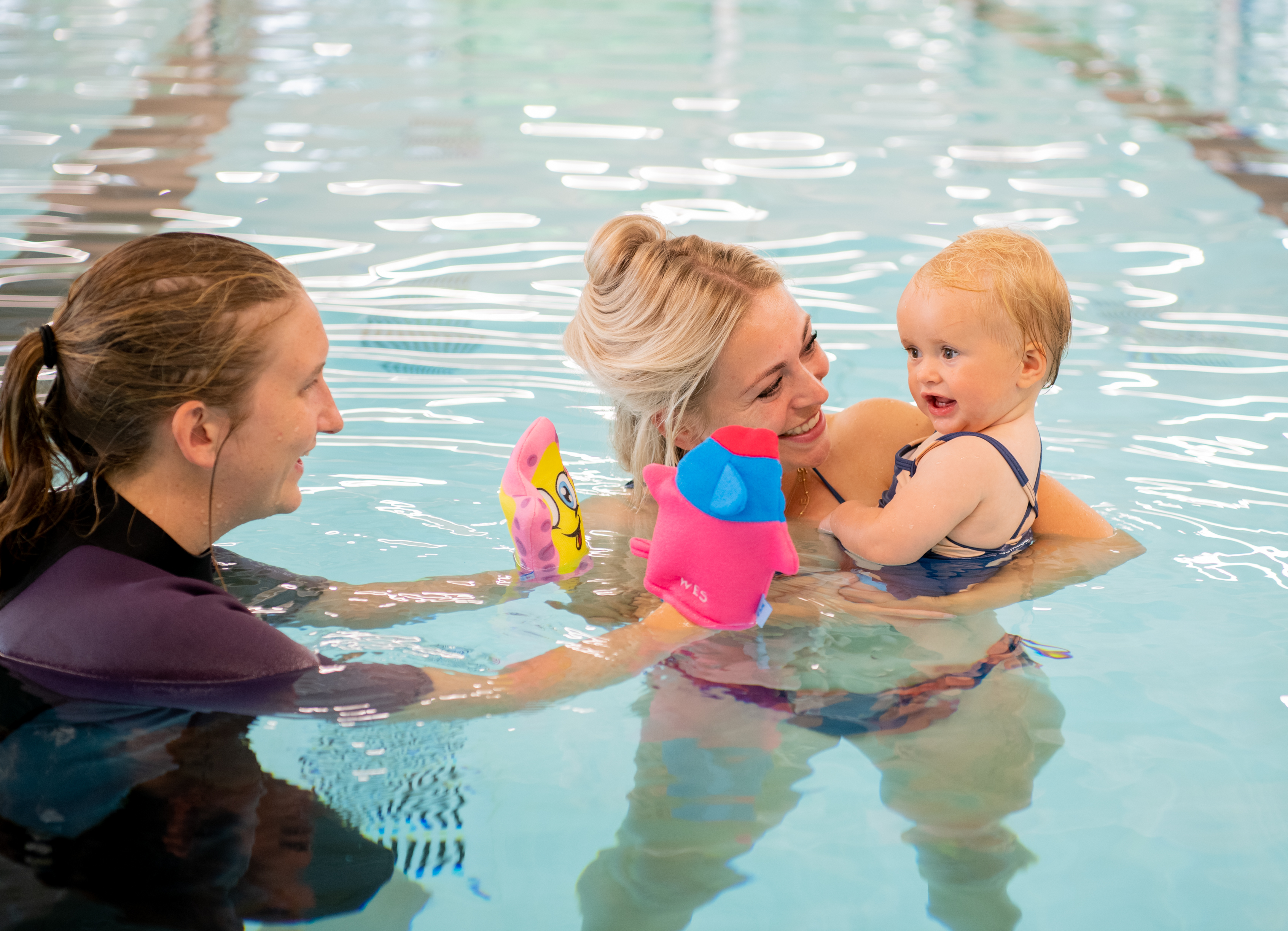 Een kind is vrolijk in het water bezig terwijl de instructeur van Optisport hierbij is.