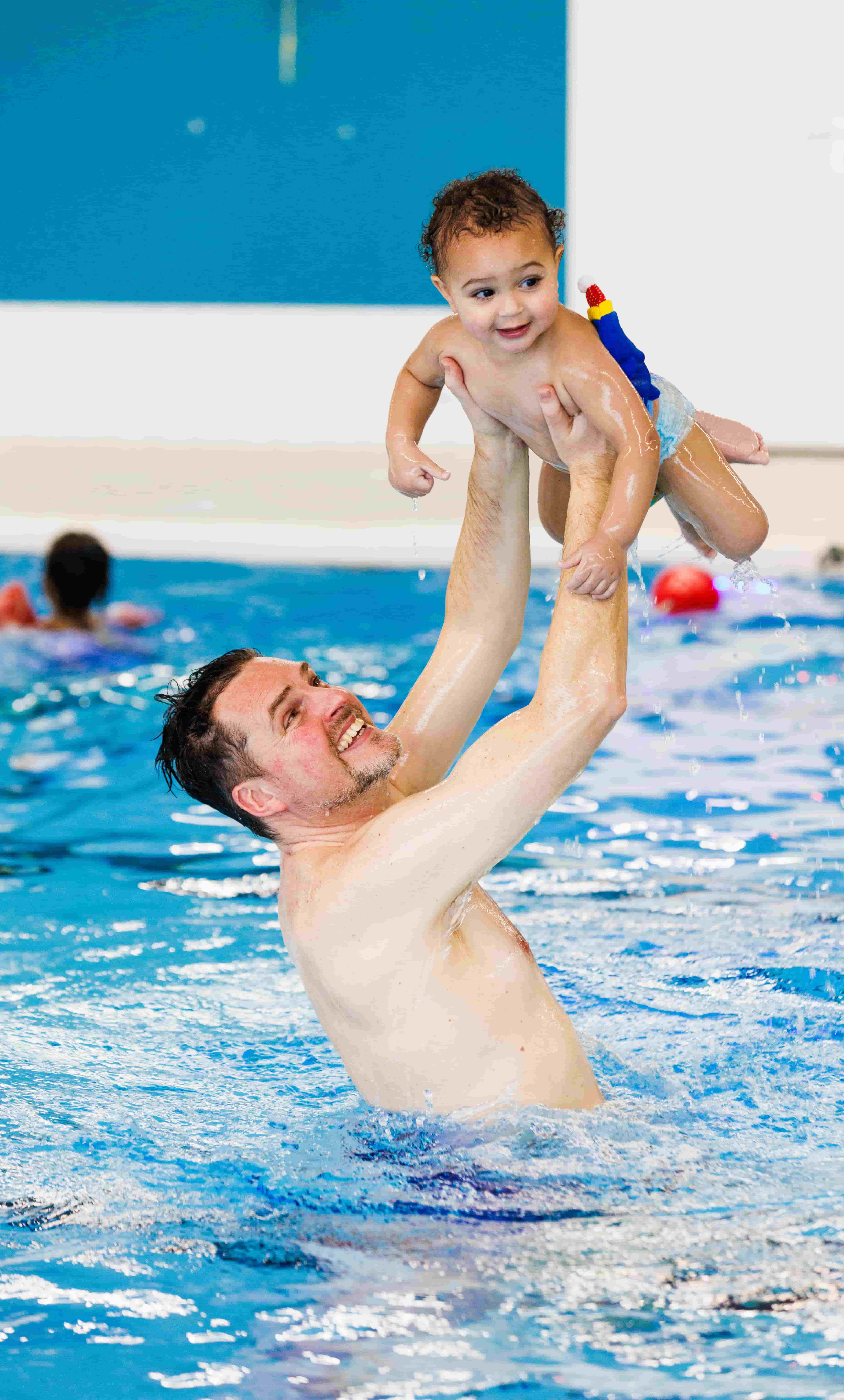 Een vader houdt zijn kind hoog in de lucht tijdens de Liz & Wes Spetterles in het zwembad van Optisport. 