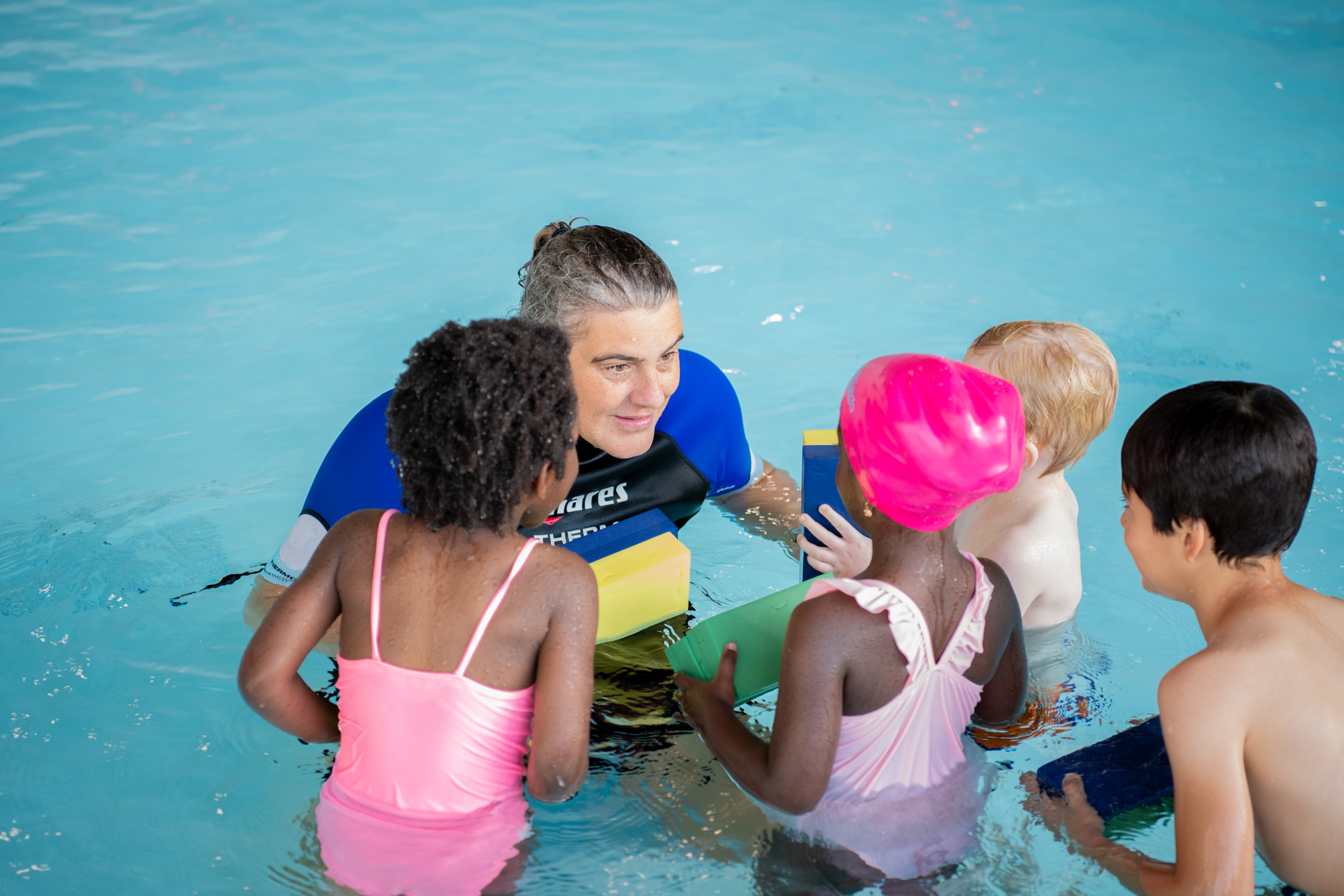 Een kind is vrolijk in het water bezig terwijl de instructeur van Optisport hierbij is.