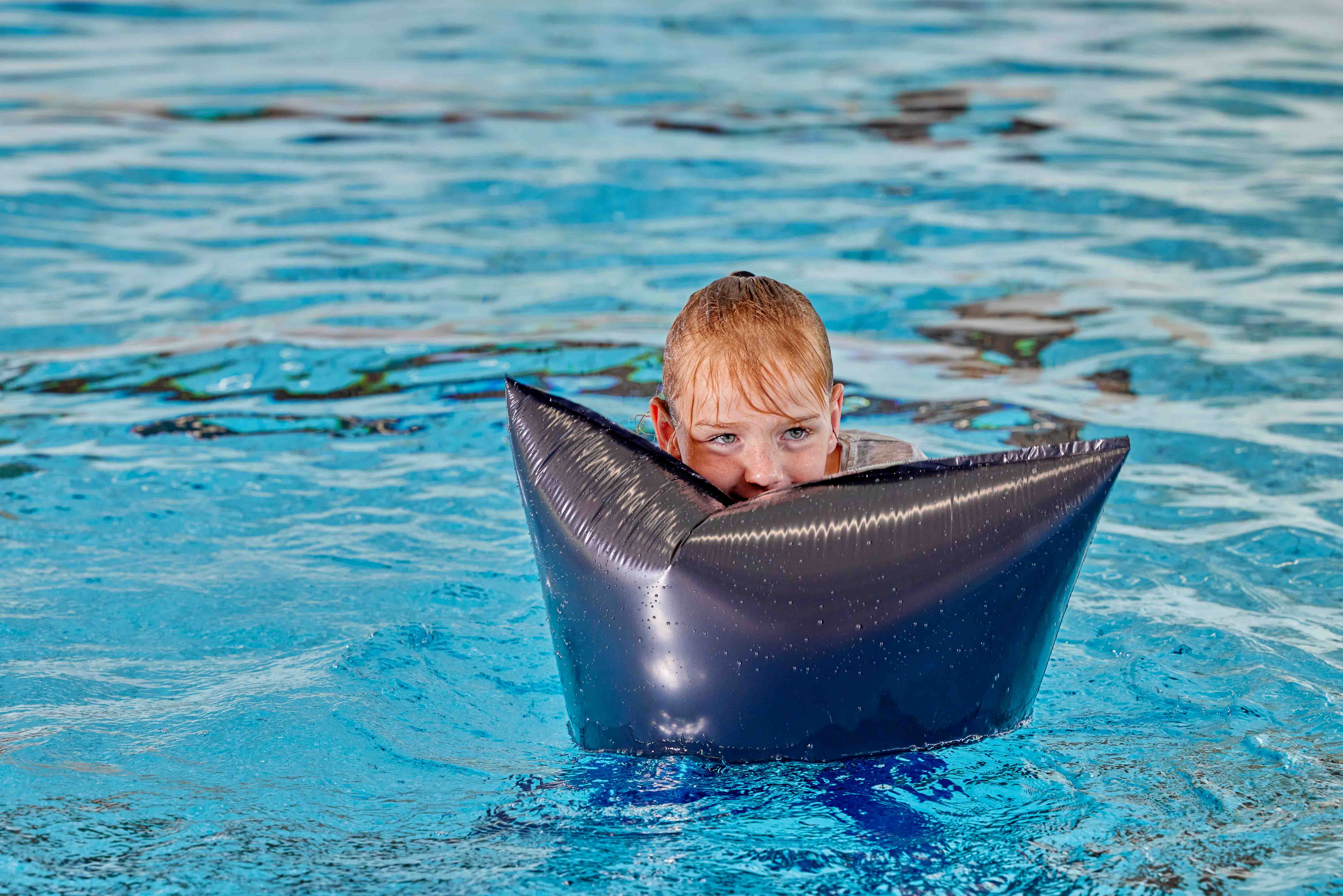 Een meisje kijkt dromerig opzij terwijl ze op een drijver ligt in het wilde water tijdens een les Survival Zwemvaardigheid bij Optisport. 