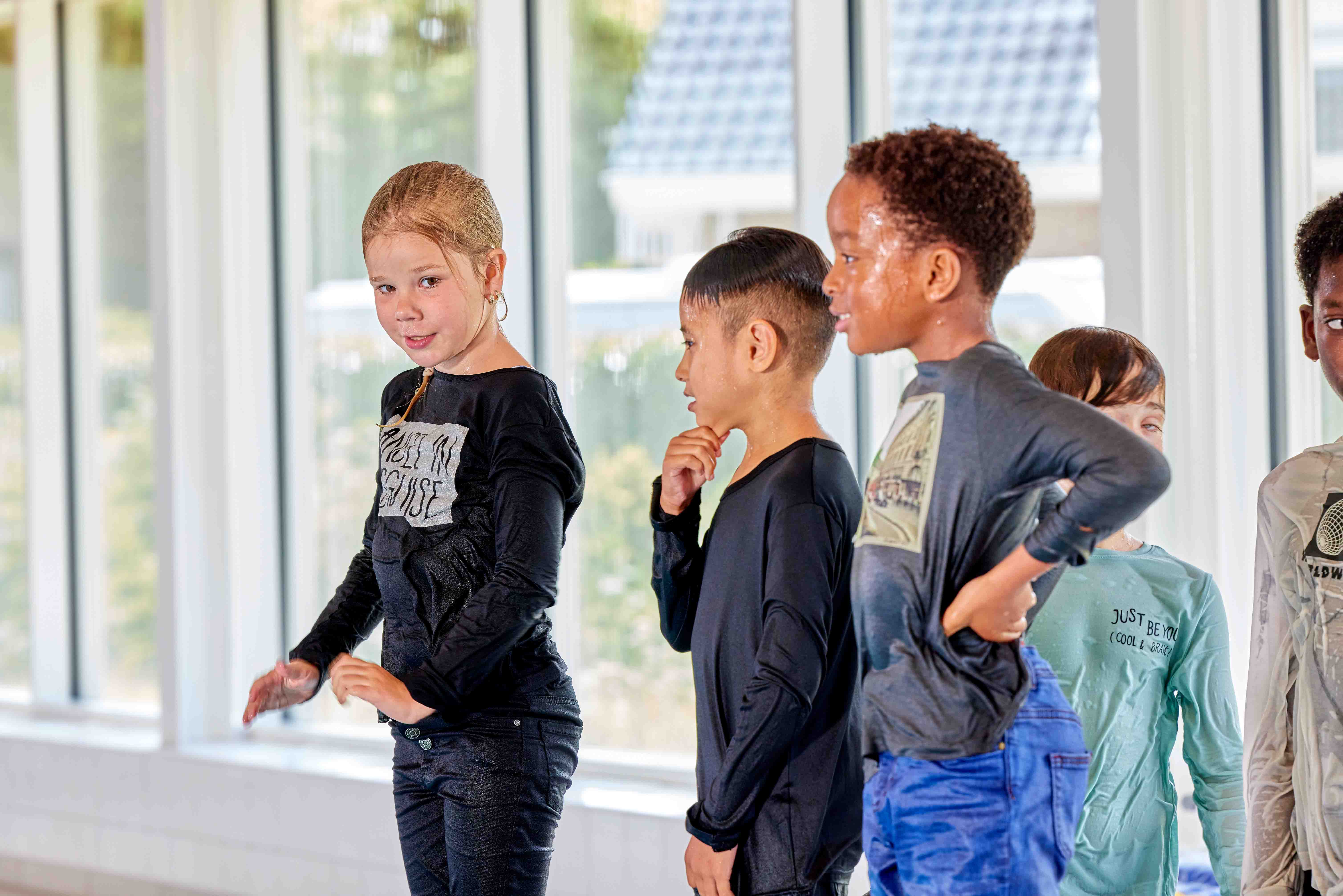 Kinderen staan, met kleding aan, in de rij om van de kant af het water in te springen tijdens de zwemles bij Optisport. 