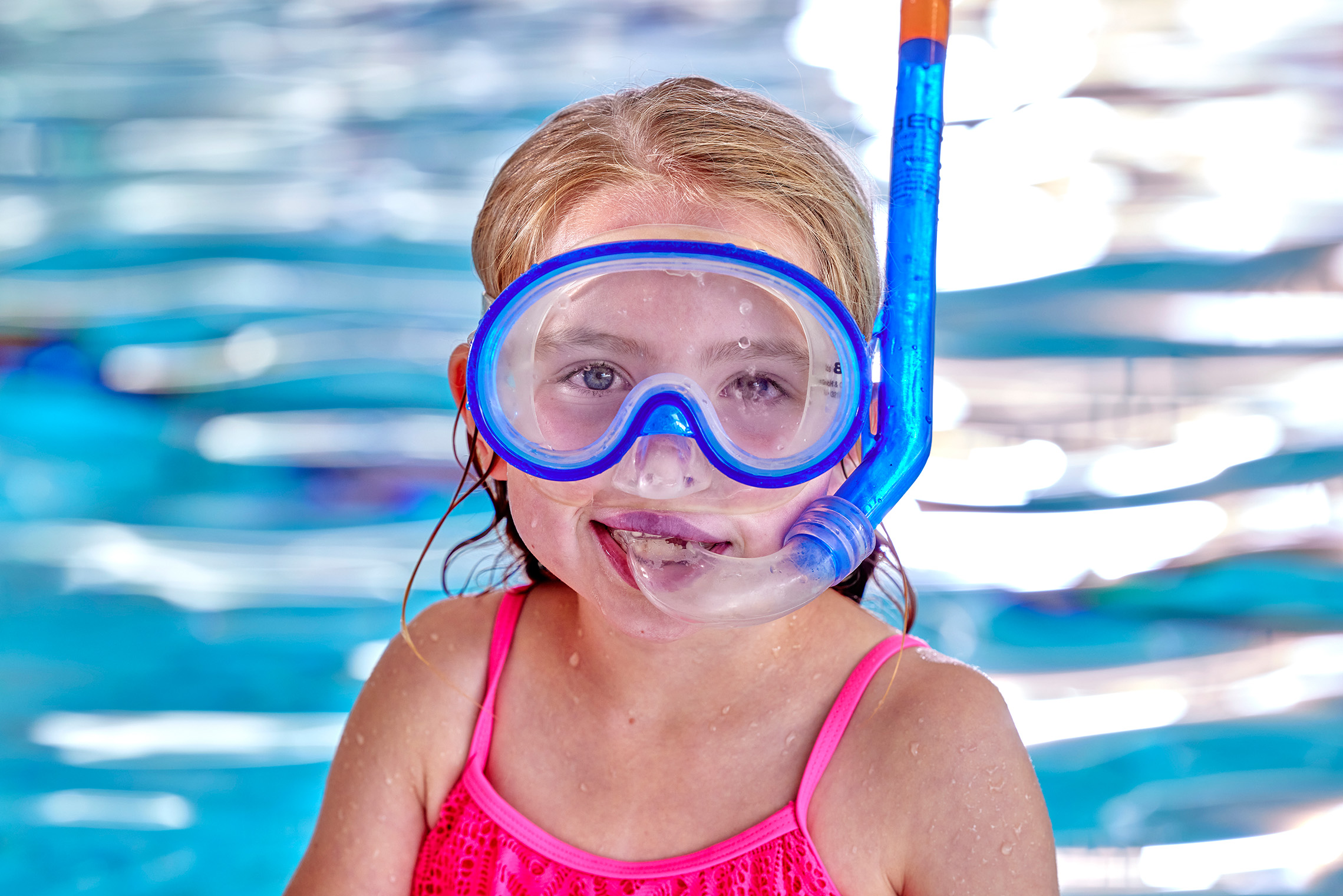 Trots kijkt een meisje met haar duikbril en snorkel op in de camera, tijdens de les Snorkelen in het zwembad van Optisport.