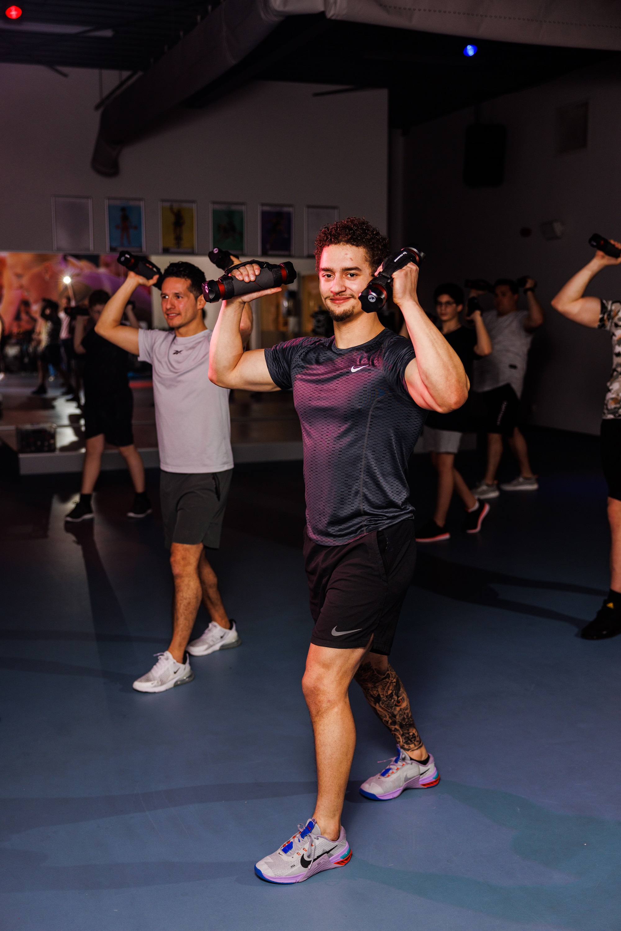 Twee mannen tillen halters boven hun hoofd tijdens een dynamische workout op een van de healthclubs van Optisport. 