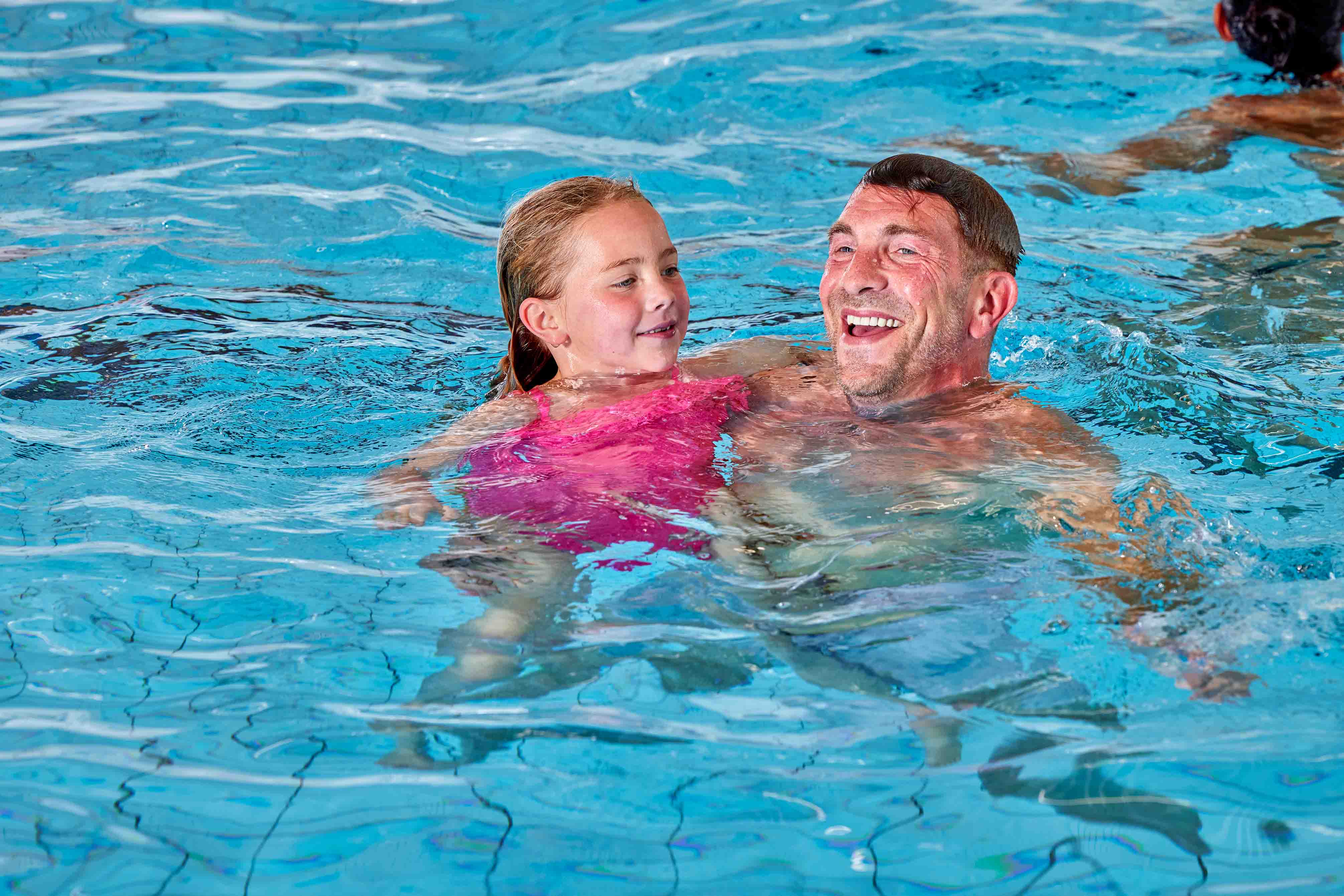 Een meisje zwemt samen met zijn vader; samen spelen ze tijdens het vrijzwemmen bij Optisport en maken veel plezier