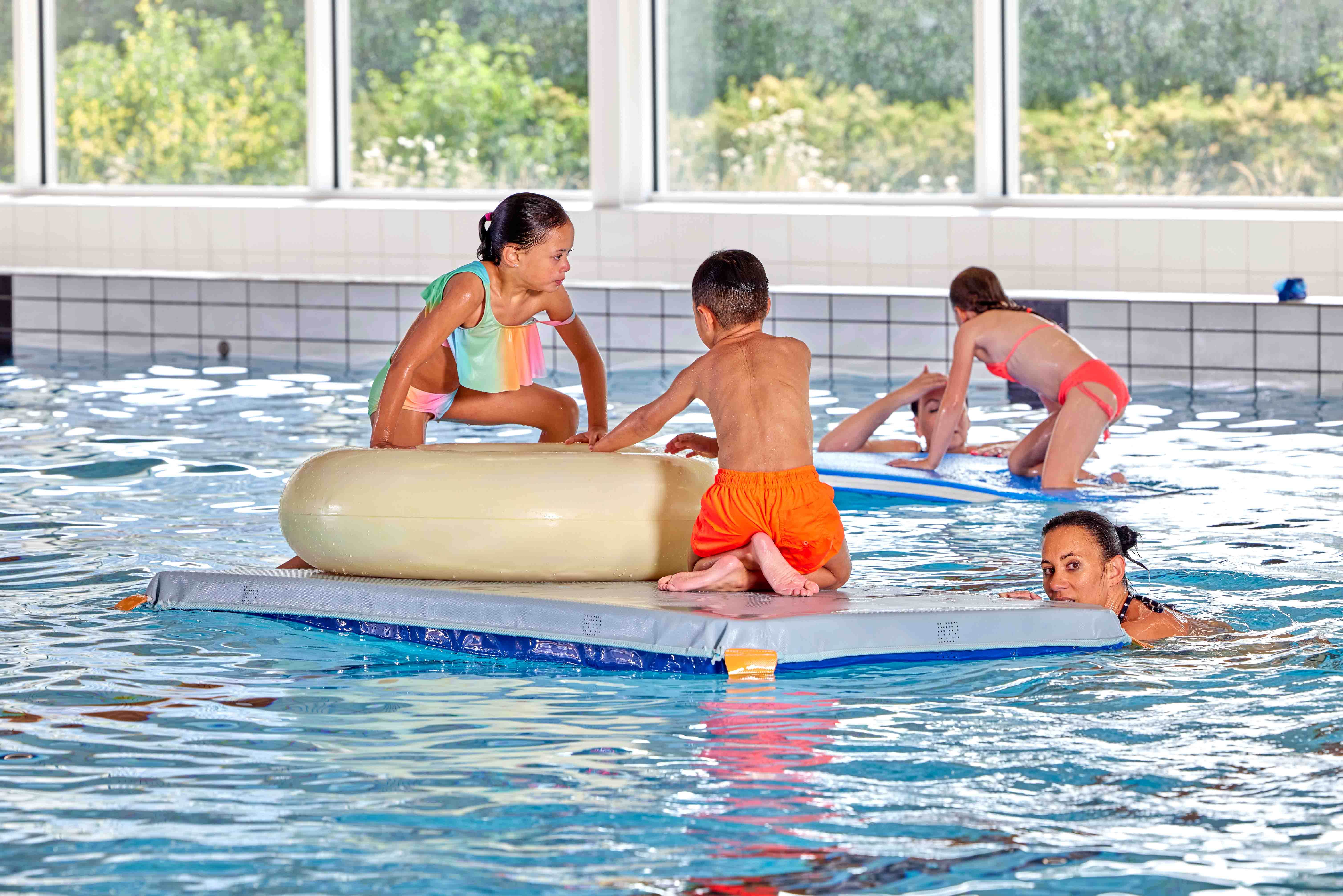 Tijdens het vrijzwemmen bij Optisport genieten diverse kinderen van alle speelmaterialen in het water. Samen spelen ze uitbundig in het water.