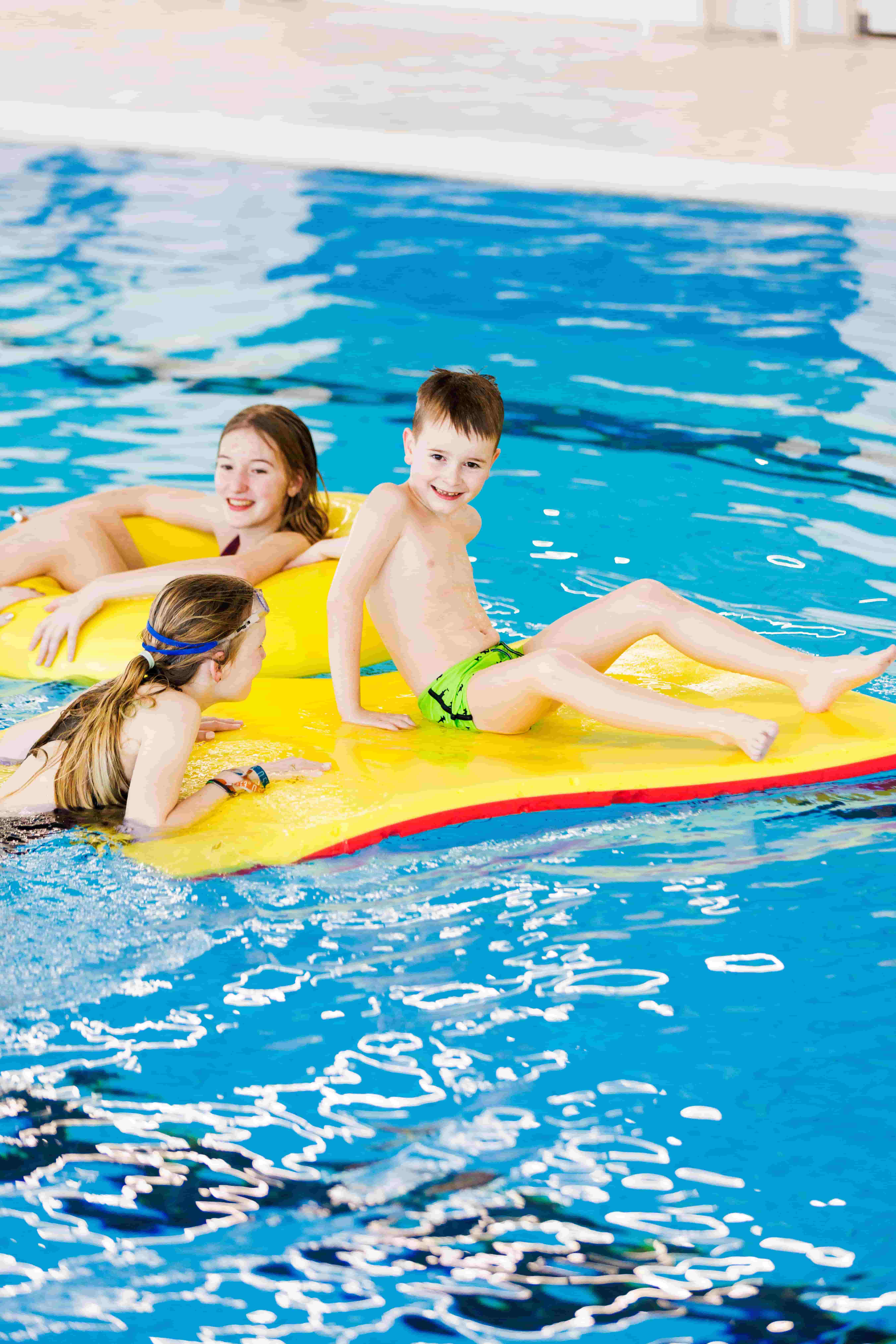 Drie kinderen spelen met diverse drijfmiddelen in het zwembad van Optisport tijdens het Vrijzwemmen. 