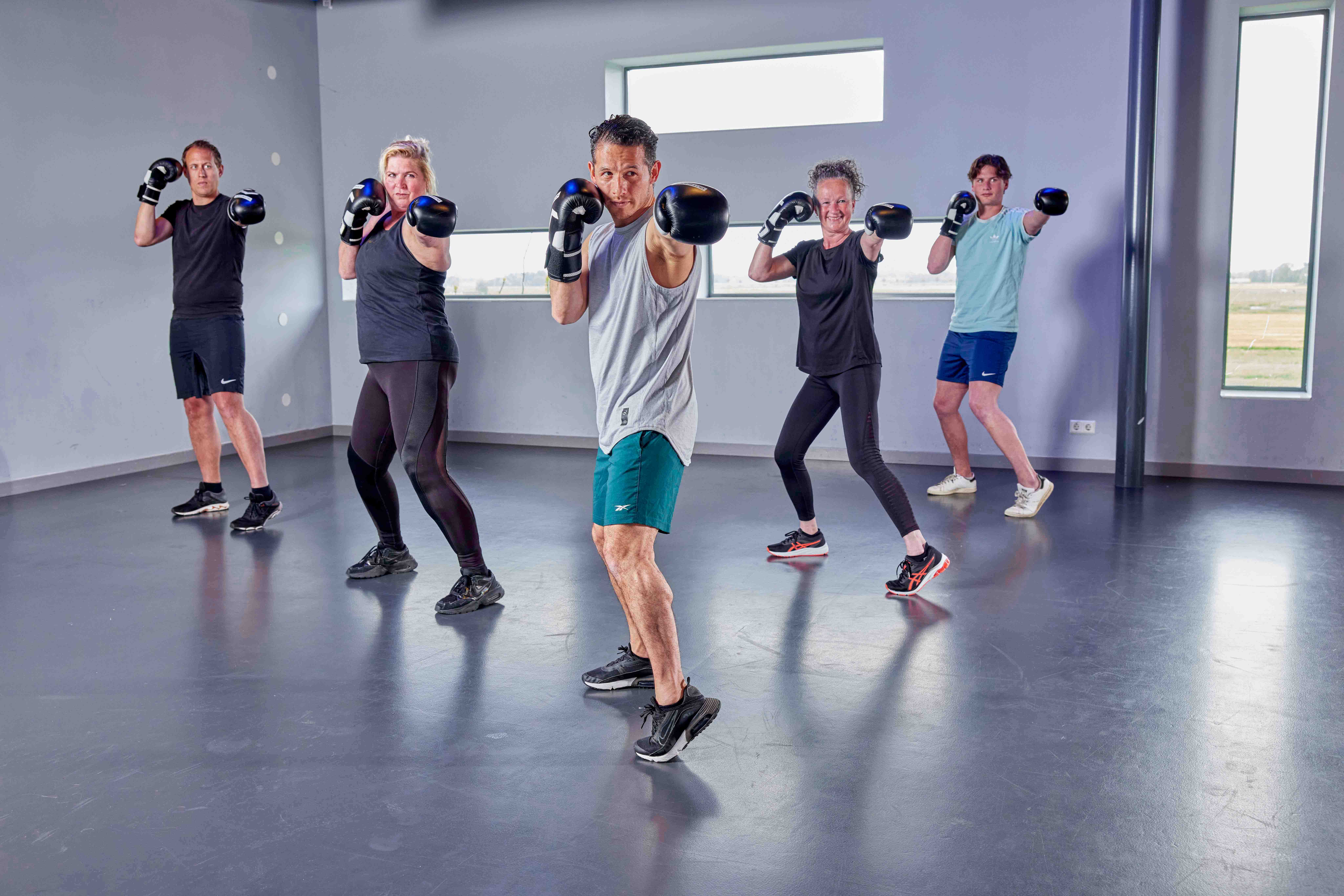 Vijf mensen staan met geheven bokshandschoenen klaar om met jou samen een botje te boksen bij een healthclub van Optisport! 