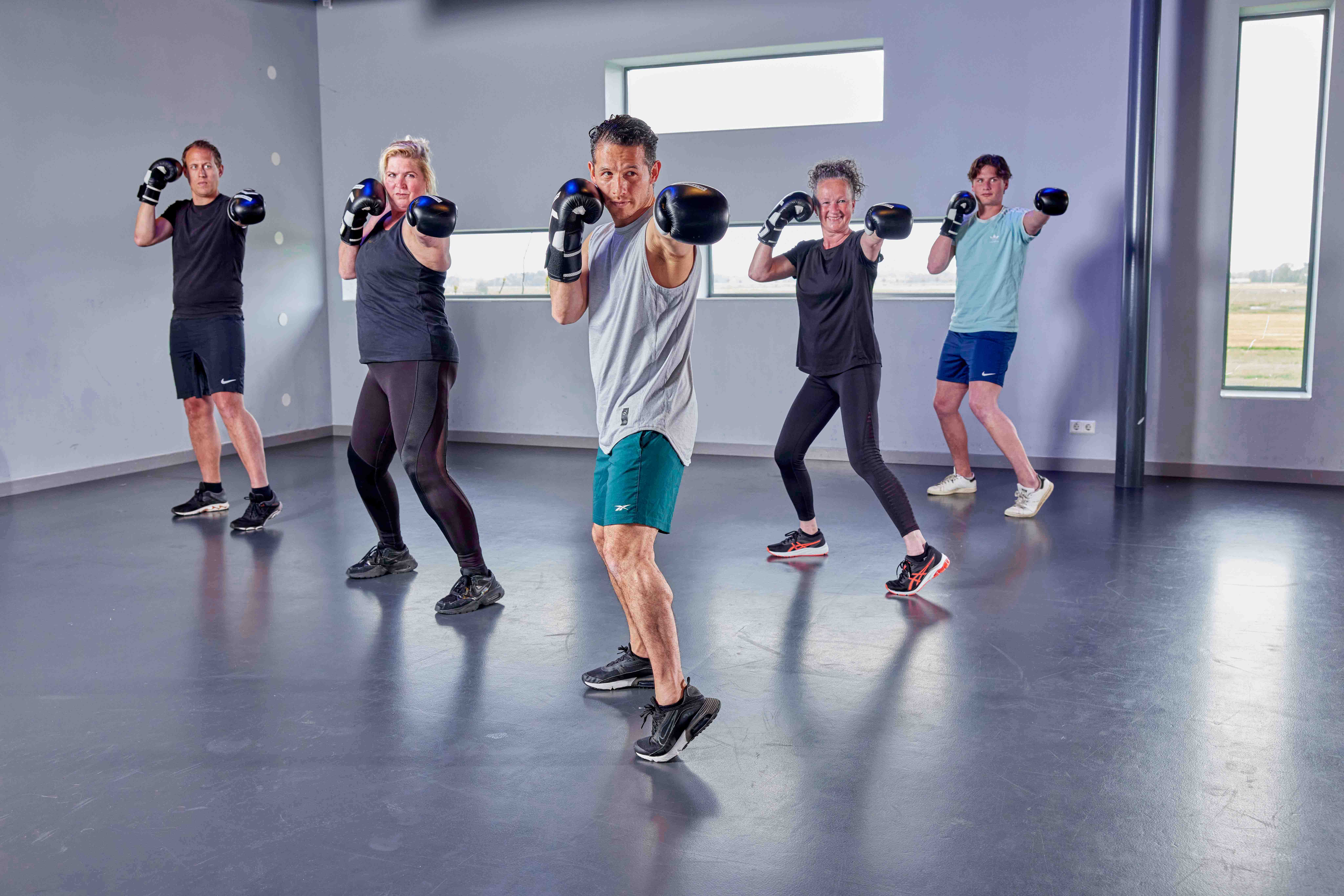 Vijf mensen staan met geheven bokshandschoenen klaar om met jou samen een botje te boksen bij een healthclub van Optisport!
