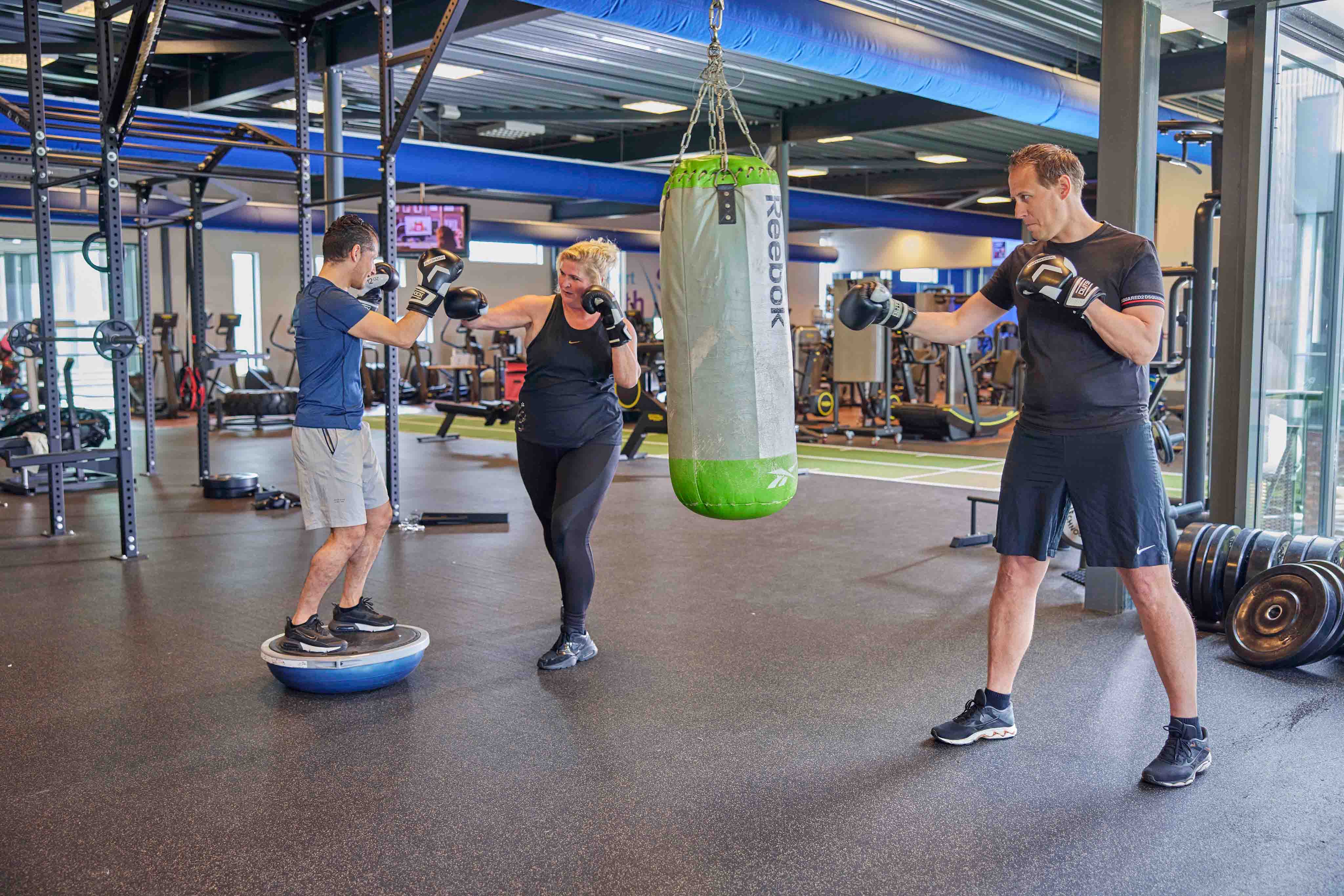 Een vrouw is aan het boksen met de instructeur, tijdens een energieke boks les bij een van de healthclubs van Optisport. 