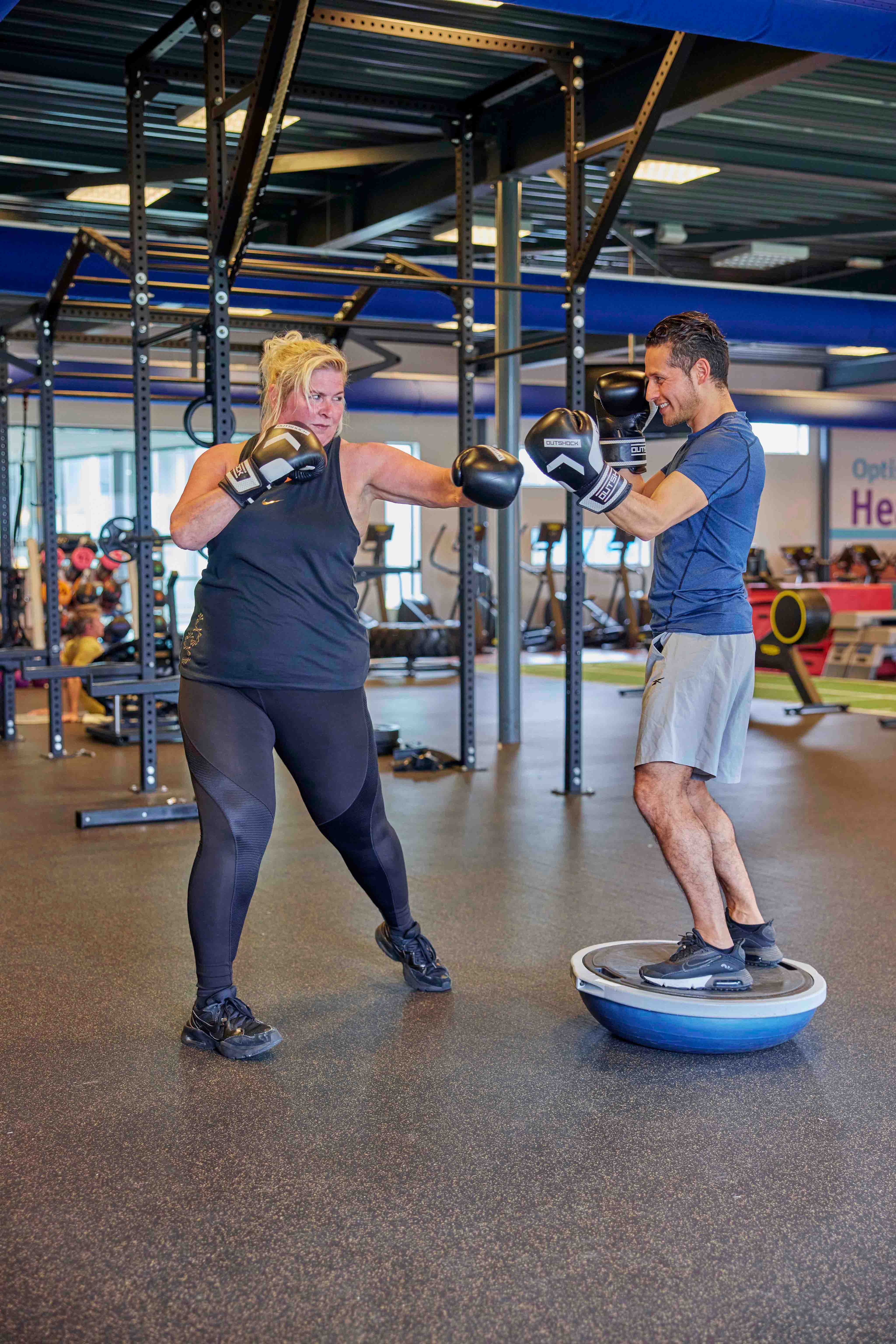 Een vrouw is aan het boksen met de instructeur, tijdens een energieke boks les bij een van de healthclubs van Optisport. 