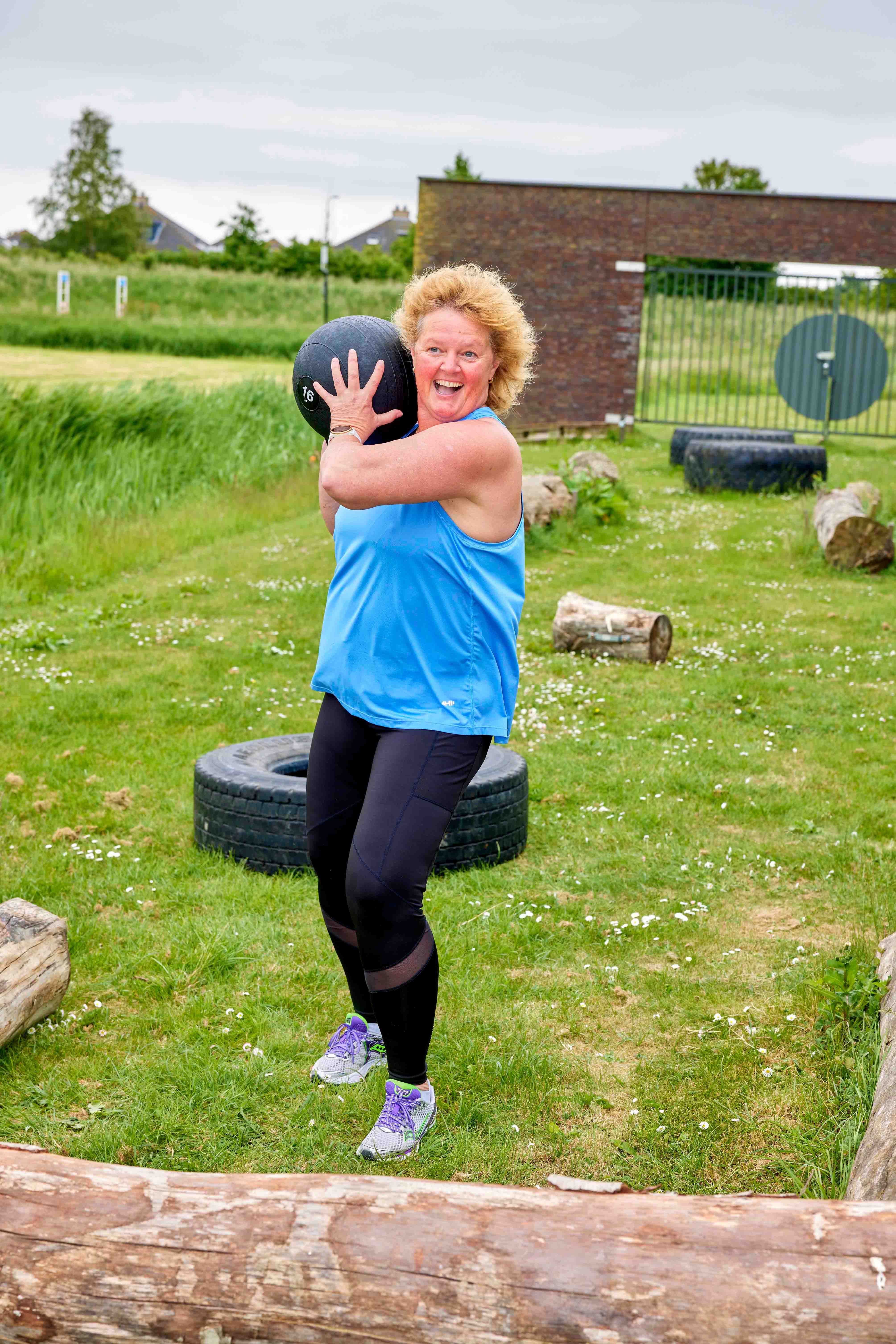 Met zichtbaar plezier doet een vrouw krachttraining met een bowlingbal tijdens de bootcamp training van een van de healthclubs van Optisport. 