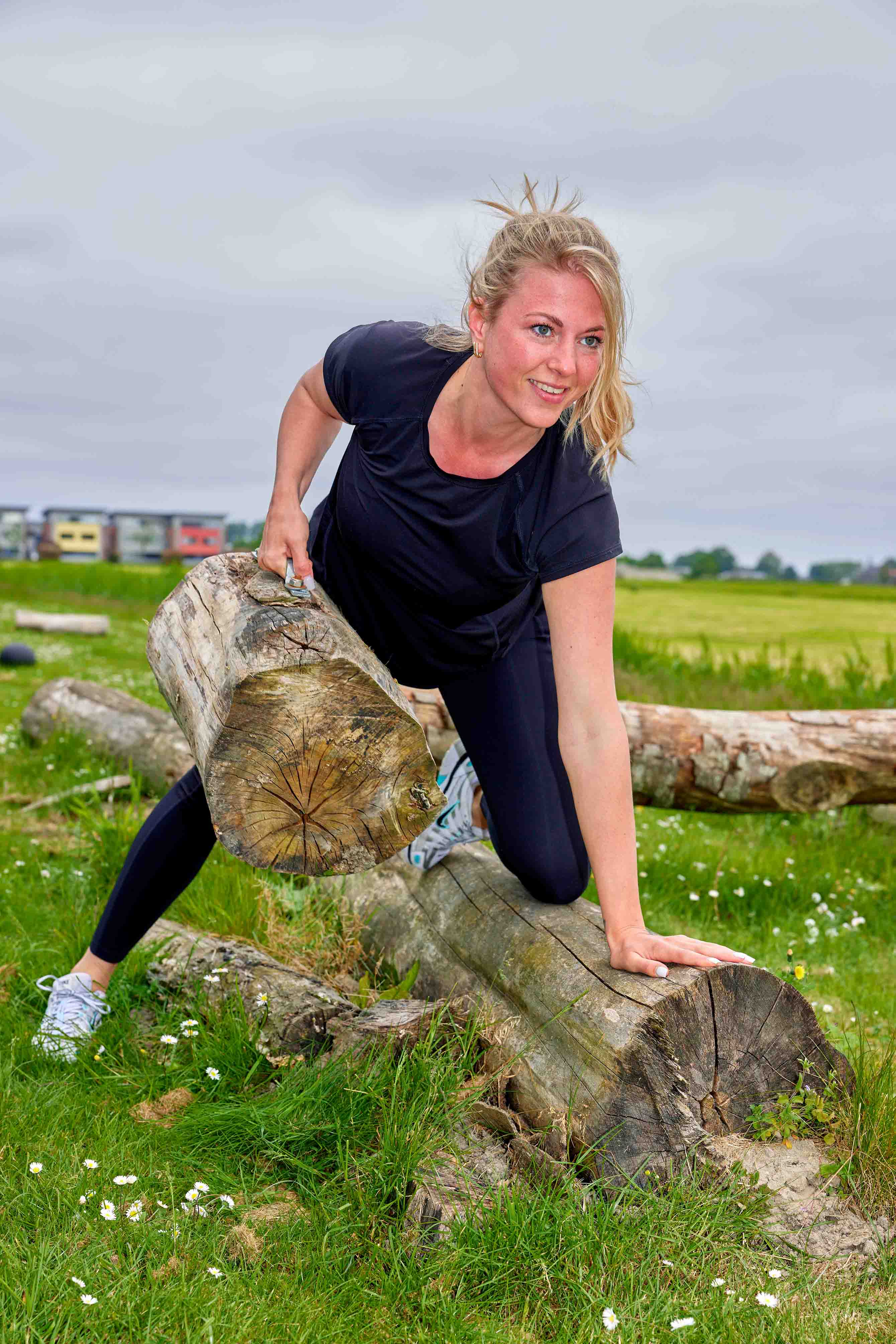 Een jonge vrouw tilt met gemak een boomstronk op tijdens een outdoor bootcamp training bij Optisport. 