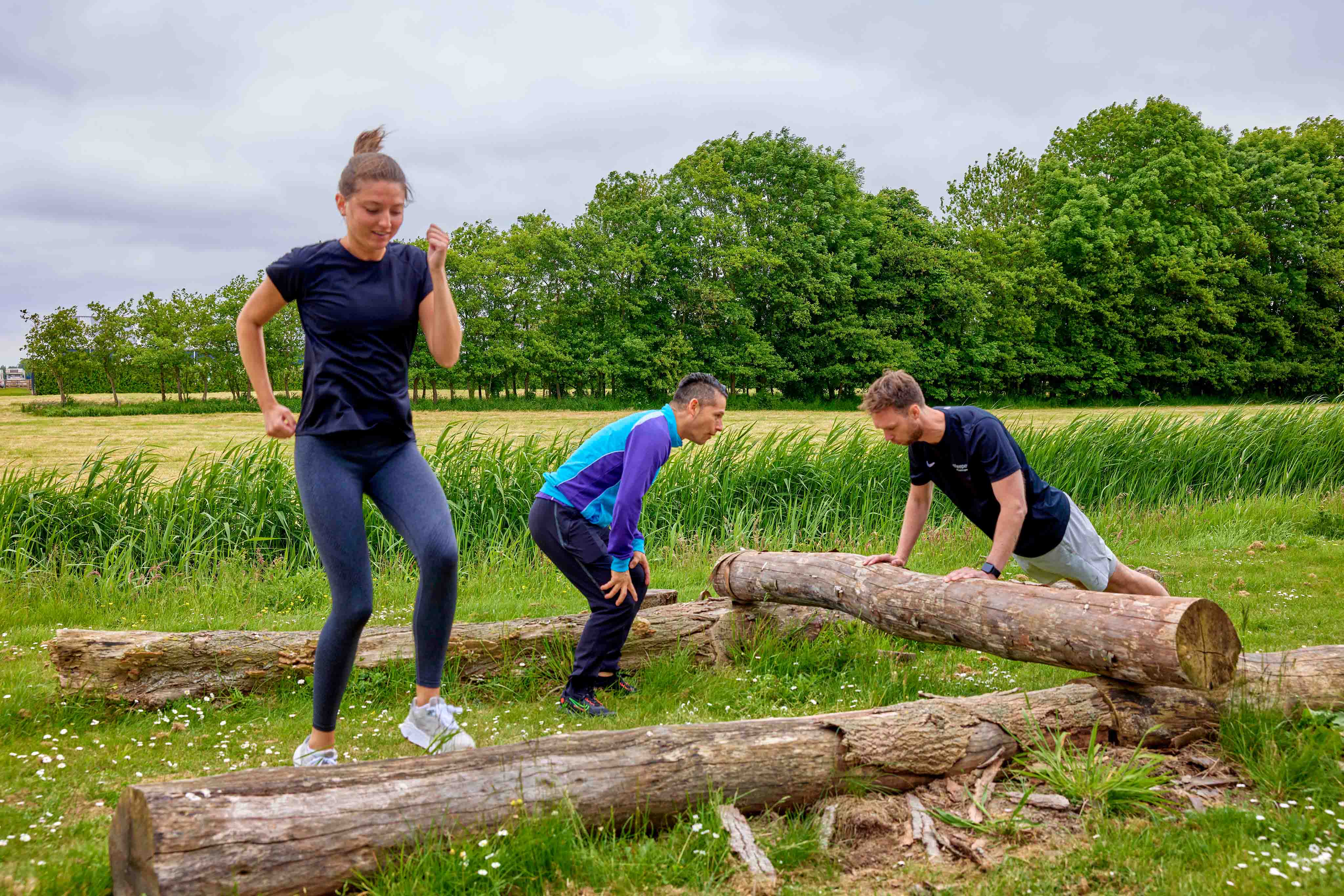 Twee sporters zijn samen heerlijk in de buitenlucht aan het trainen onder leiding van een ervaren instructeur, bij een van de Optisport healthclubs.  