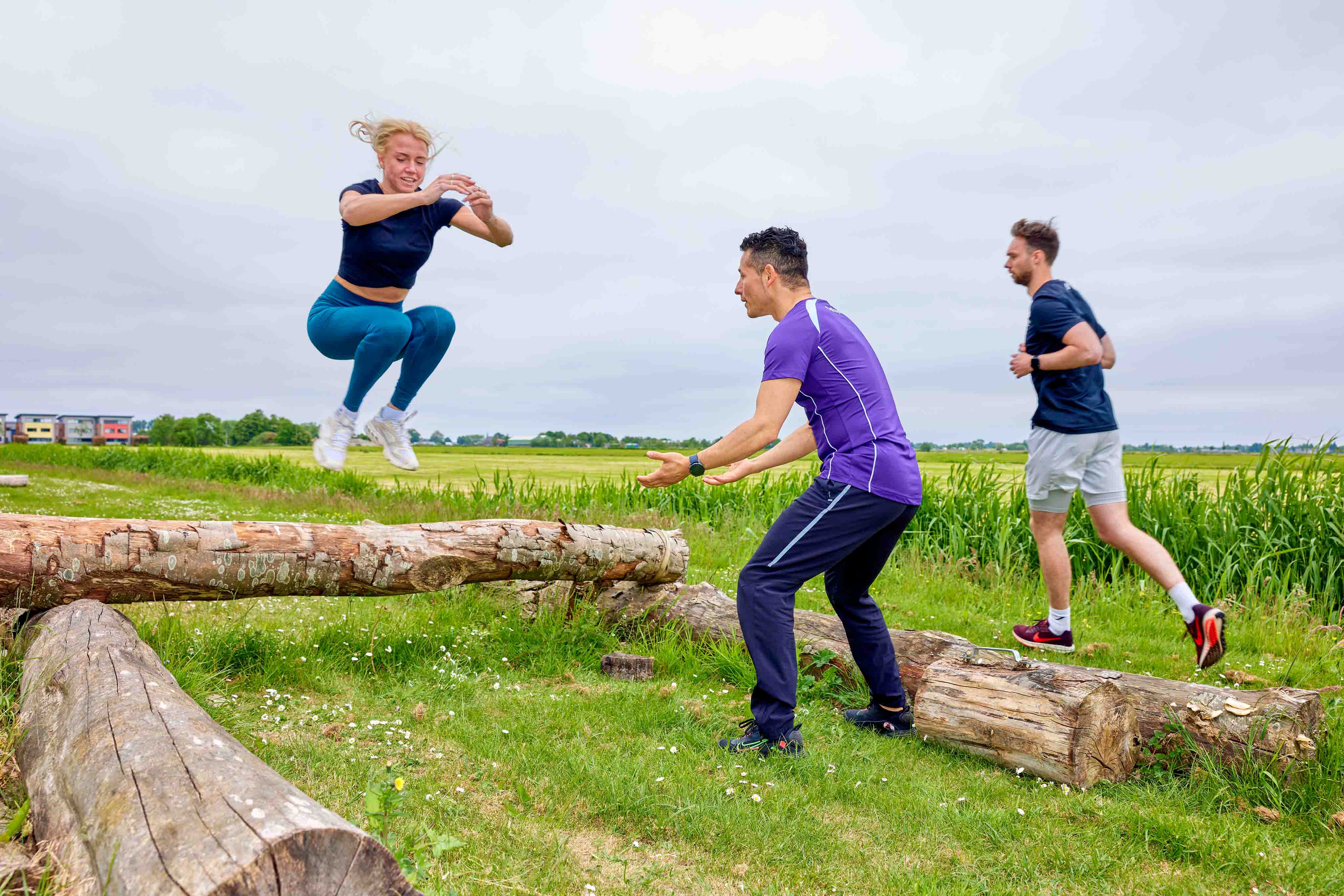 Met twee benen tegelijk springt een jonge vrouw moeiteloos over een obstakel heen, tijdens een bootcamp training bij Optisport. 