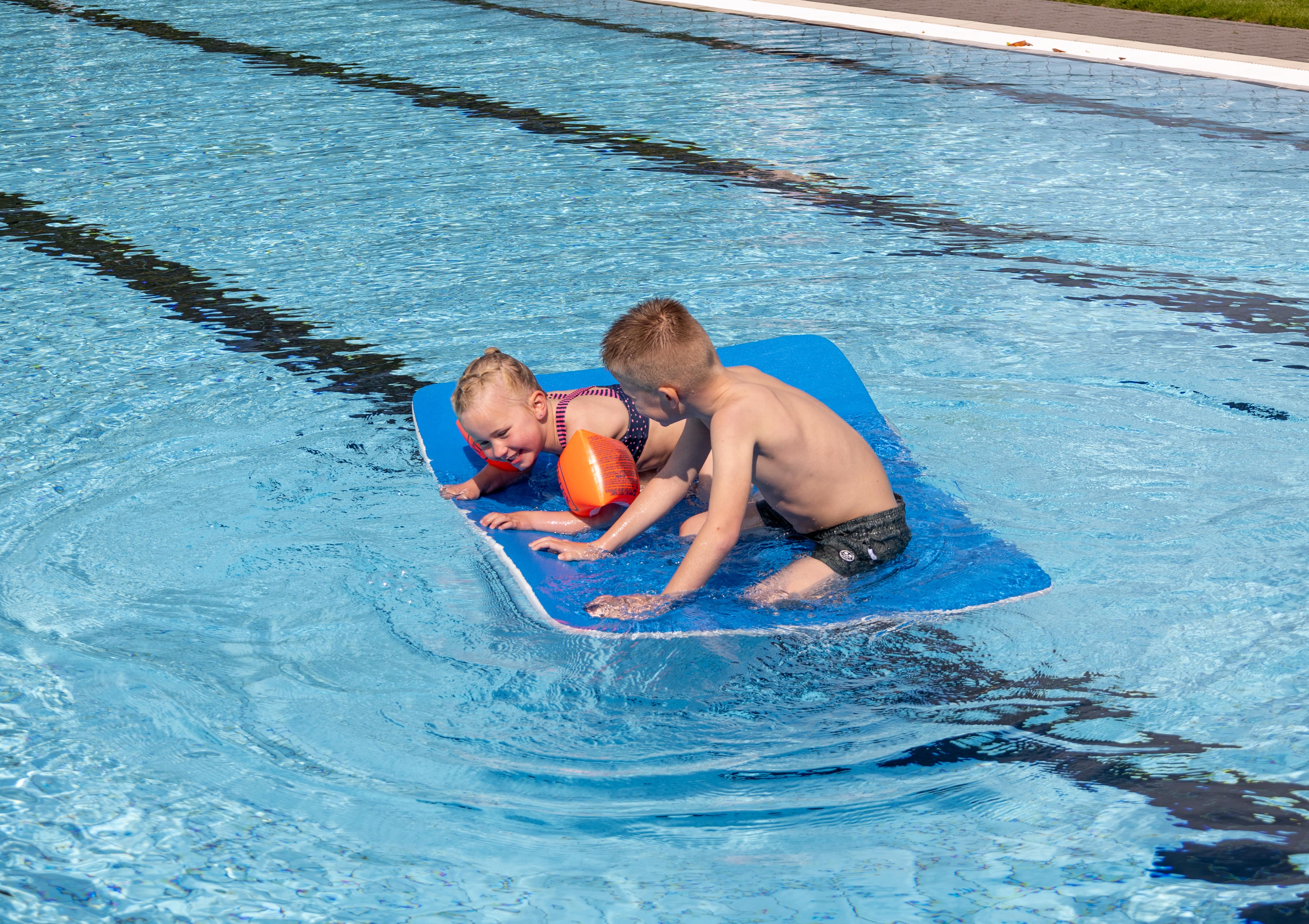Meisje met bandjes en een jongen op een blauwe mat in het water